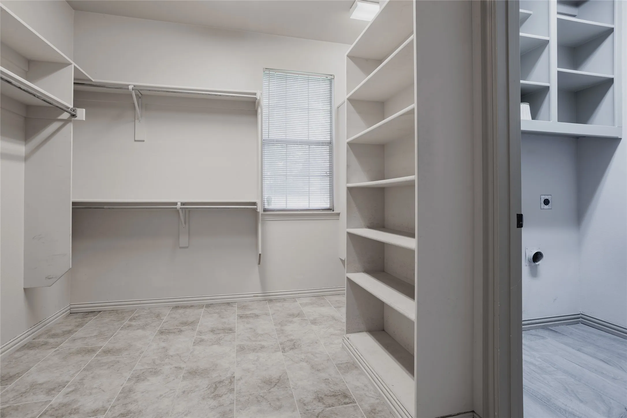 Built-in shelving, hanging rods, window, and tile flooring