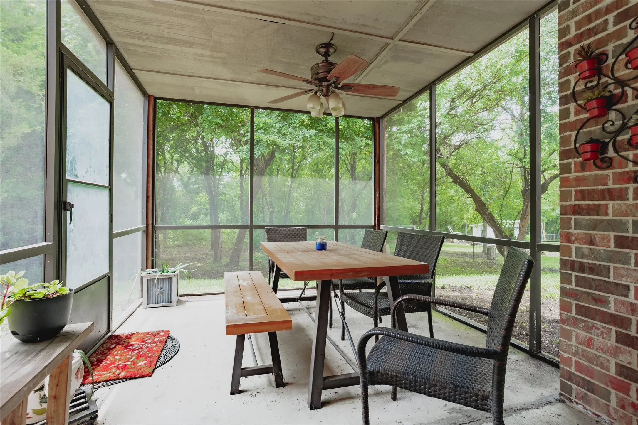 Screened porch with concrete flooring, exposed brick wall, and ceiling fan