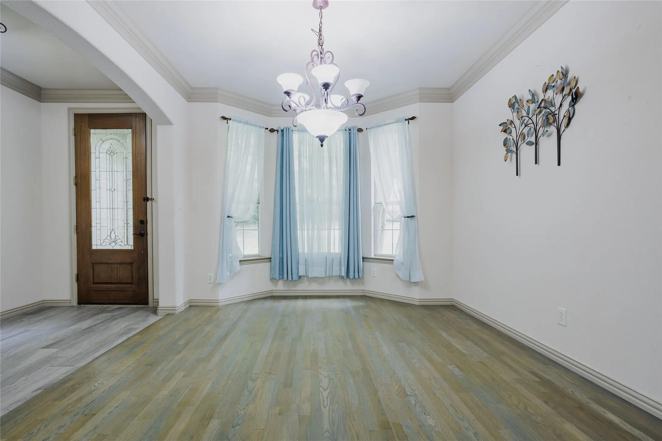 Recessed bay window, decorative chandelier, crown molding, wood-finish flooring, and a glass-paneled entry door