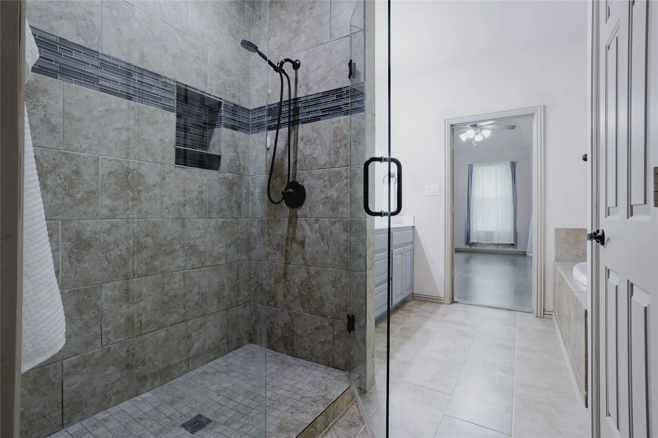 Glass-enclosed shower with a tiled floor, dark accent tile stripe, and a built-in shower niche