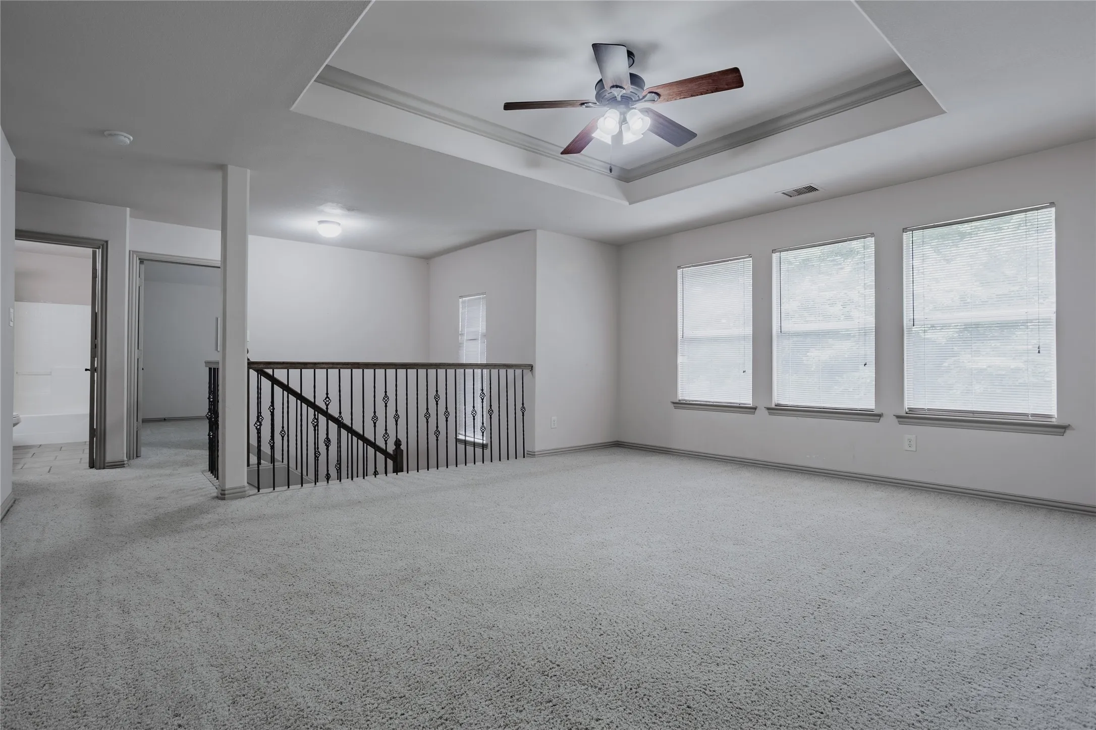 Spacious carpeted area with a tray ceiling and ceiling fan