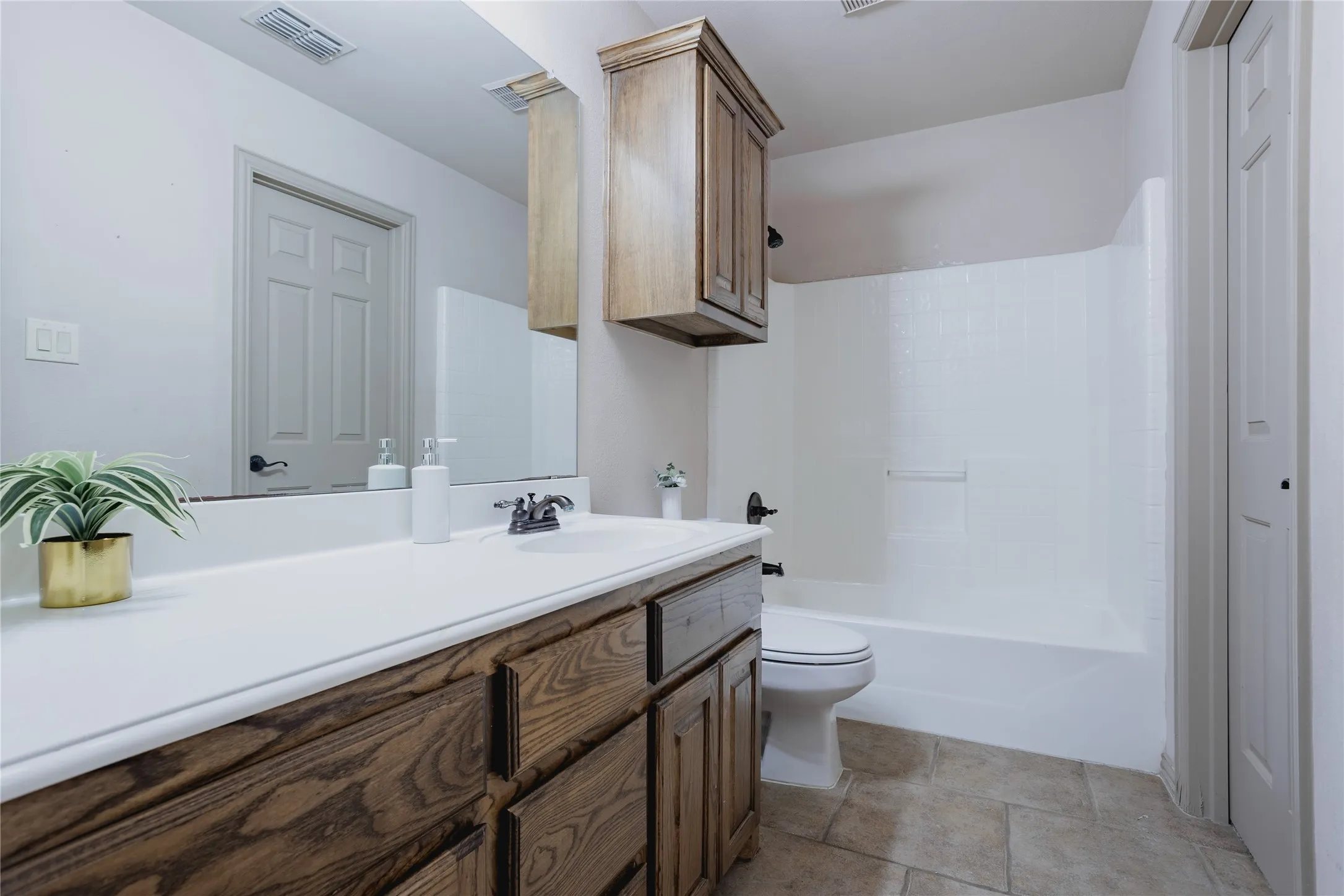 Bathroom featuring a wood-finish vanity with a white countertop, an integrated sink, a full-width mirror, and a combination tub/shower with a white surround