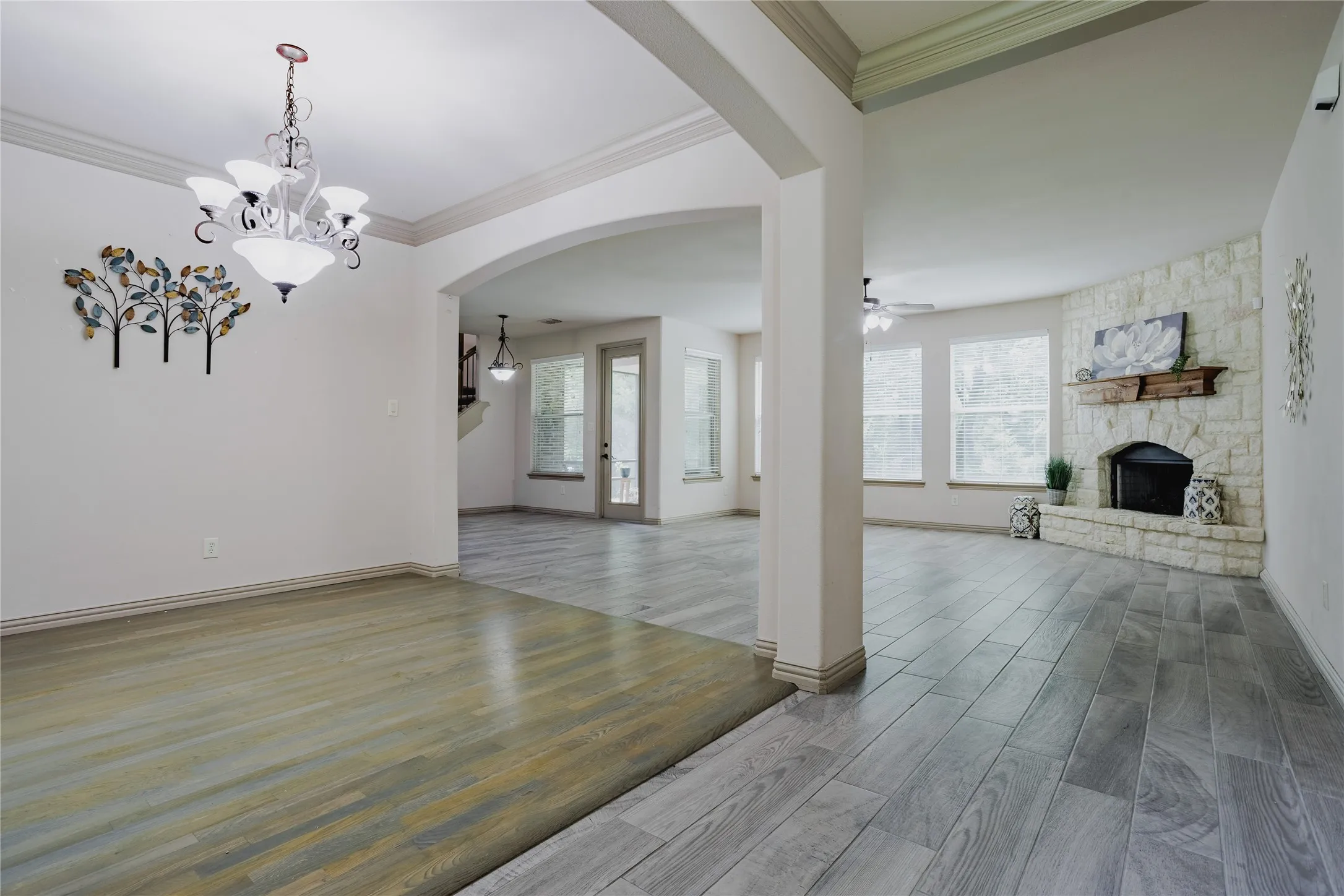 Stone-clad fireplace with wood mantel, multiple large windows, arched doorways, wood-finish flooring, and recessed lighting