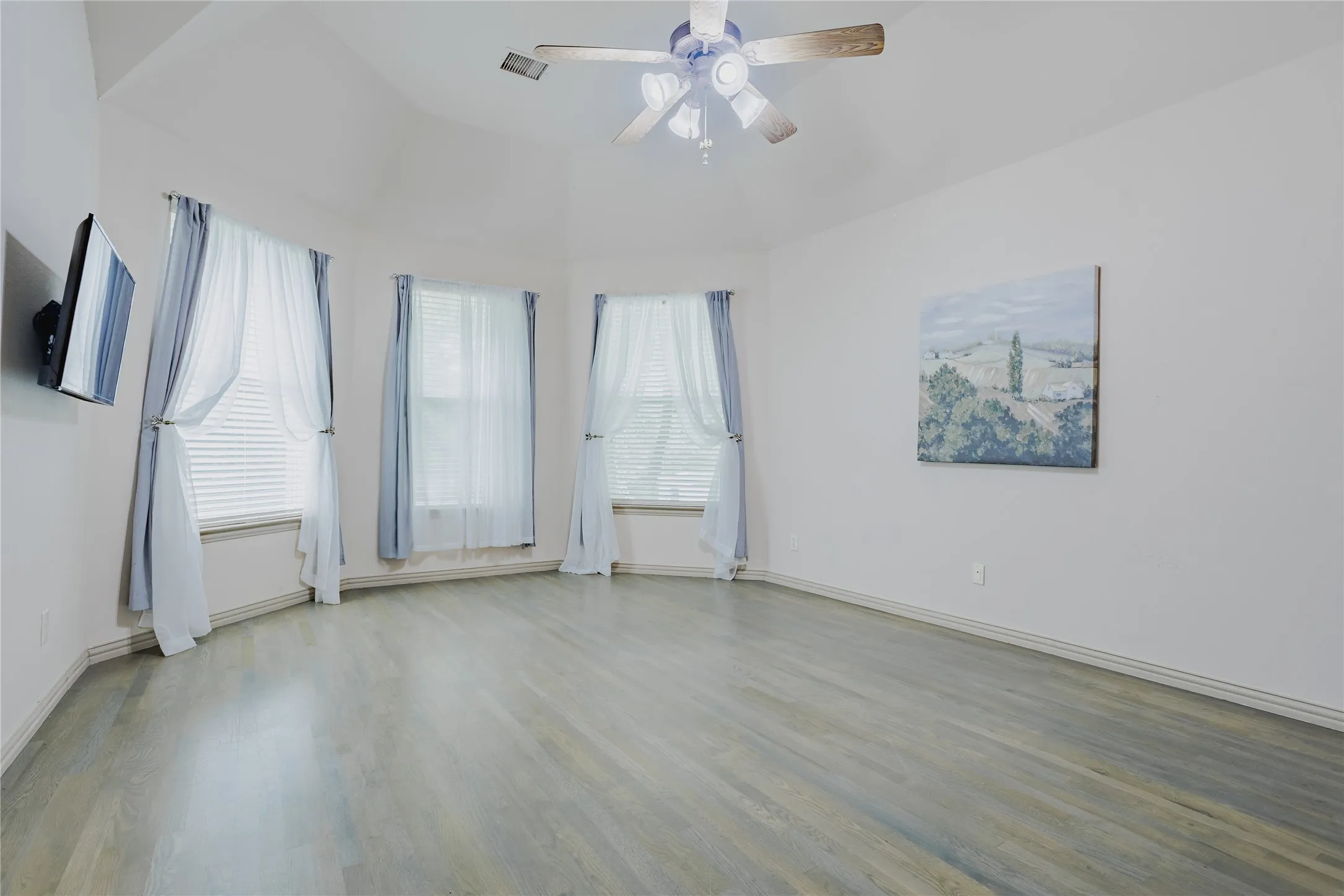 Vaulted ceilings with a ceiling fan, three windows, and wood-finish flooring