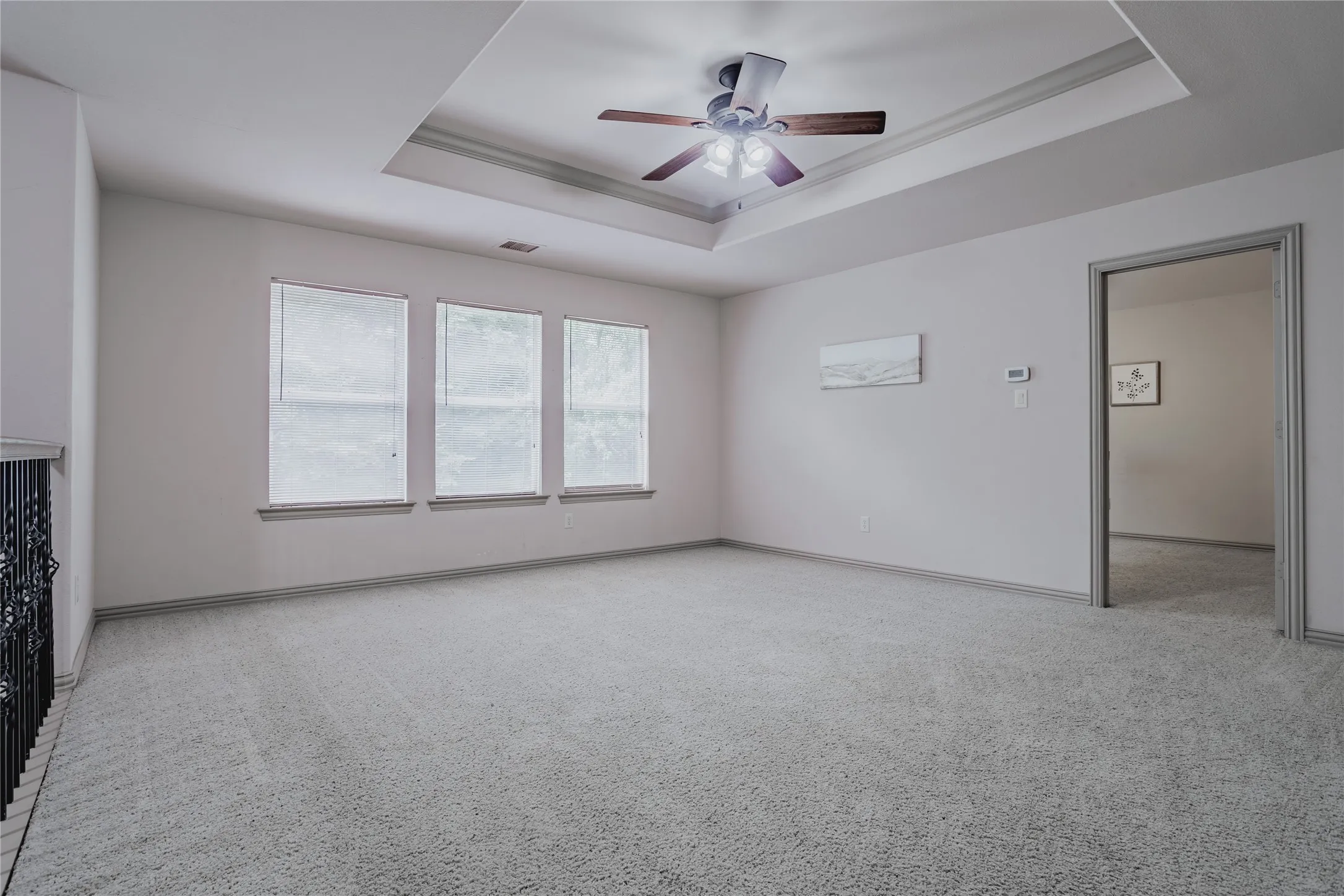 Recessed tray ceiling with a built-in ceiling fan, light gray carpeting, and three transom windows