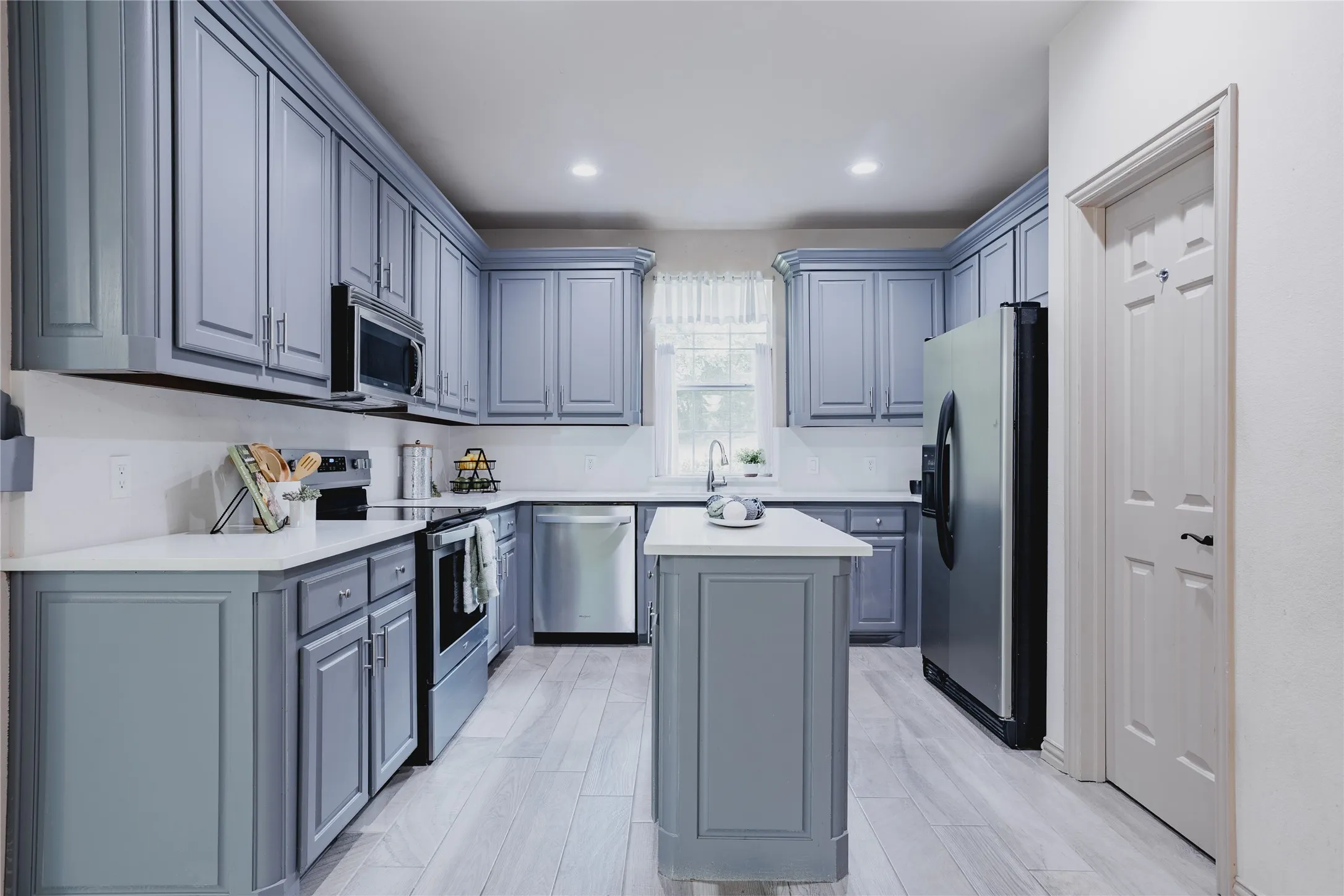 Spacious kitchen featuring extensive gray cabinetry, light-toned countertops, stainless steel appliances, a central island, and wood-finish flooring