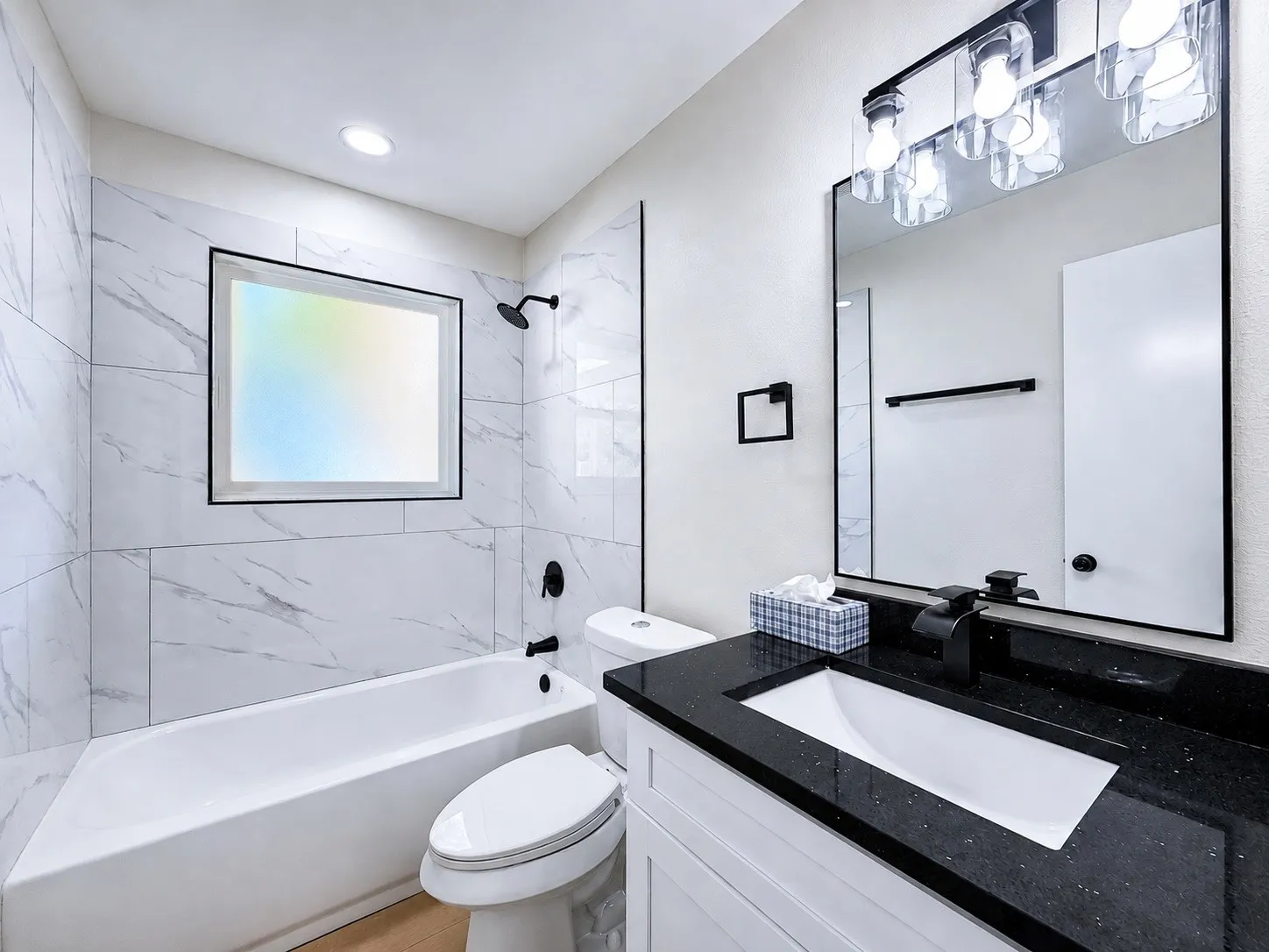 White ceramic bathtub with matte black fixtures, set against large format white marble-look wall tiles
