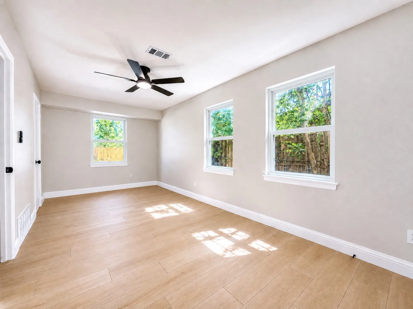 Wood-finish flooring, multiple windows, a ceiling fan with integrated lighting, and white trim