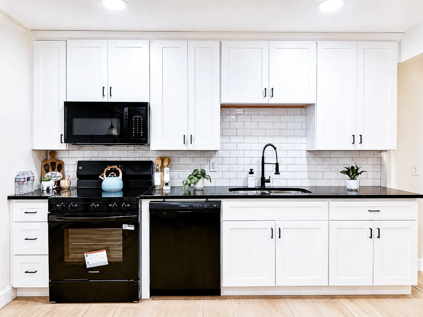 White shaker-style cabinetry, black countertop, subway tile backsplash, black kitchen appliances, and wood-finish flooring