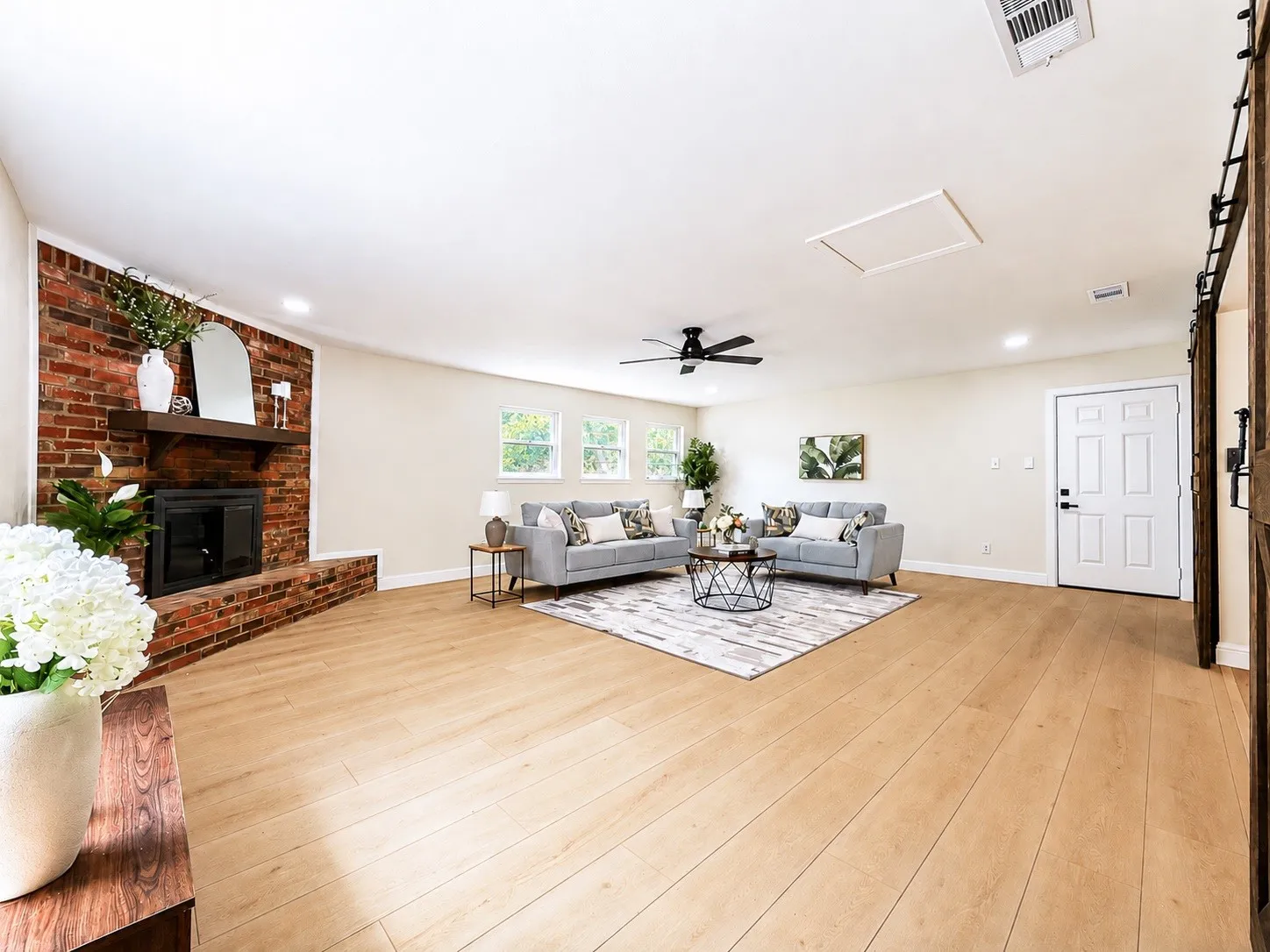 Spacious living area featuring a brick fireplace, wood-finish flooring, a ceiling fan, recessed lighting, and multiple windows