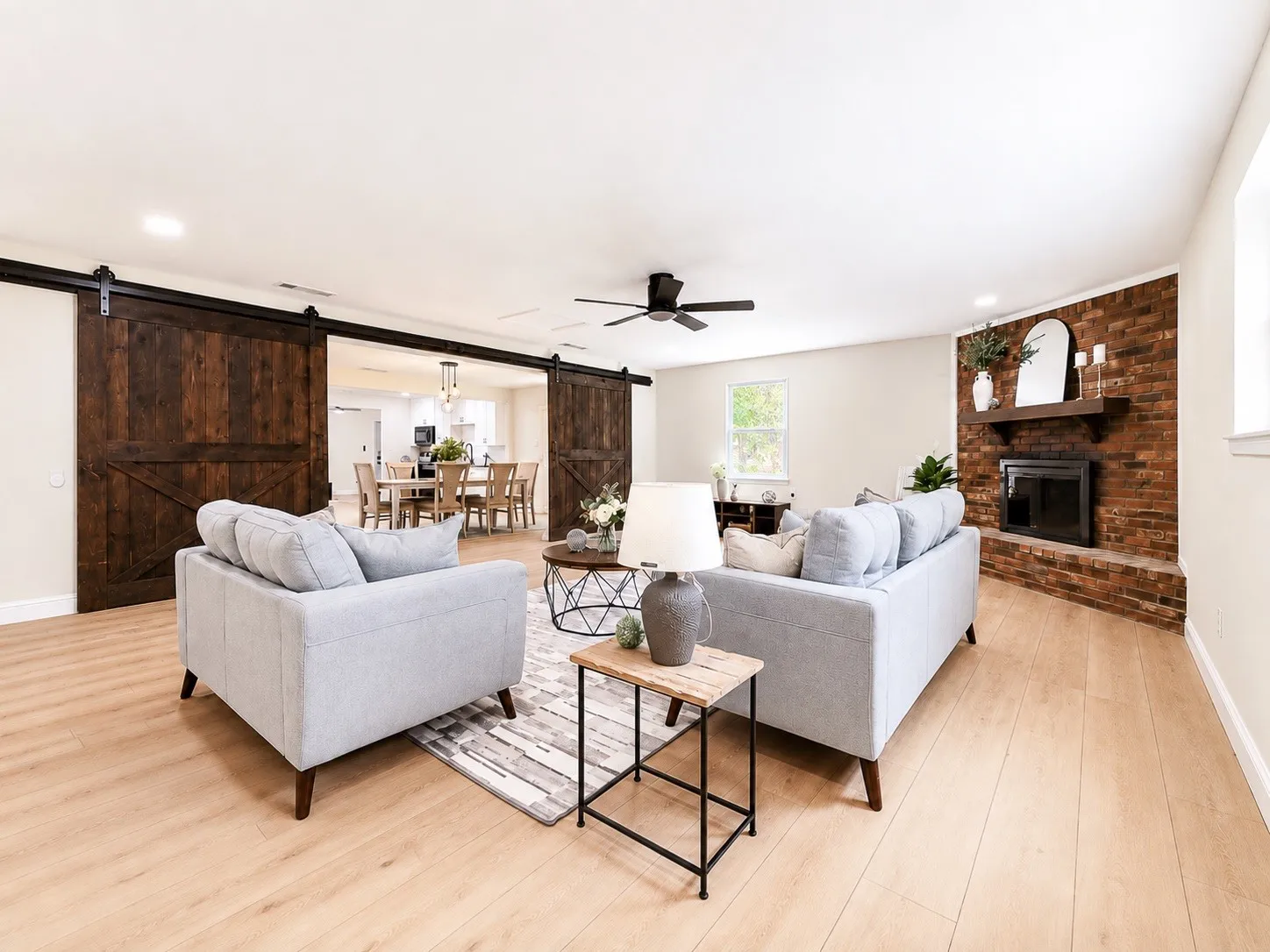 Wood-finish flooring, exposed brick fireplace, built-in ceiling fan, and dark wood barn doors