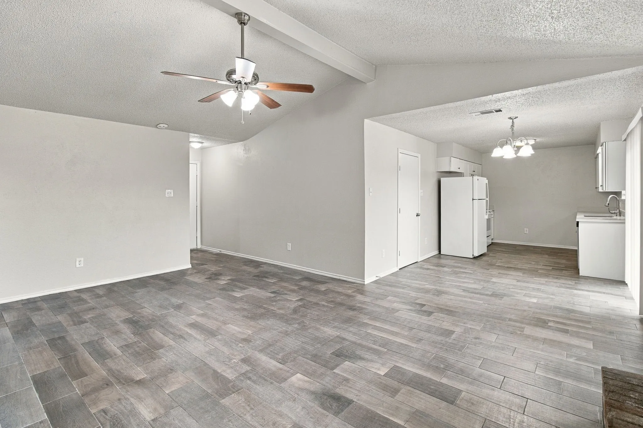 Vaulted ceiling with exposed beam, wood-finish flooring, ceiling fan, recessed lighting, and a kitchen with white appliances and cabinetry