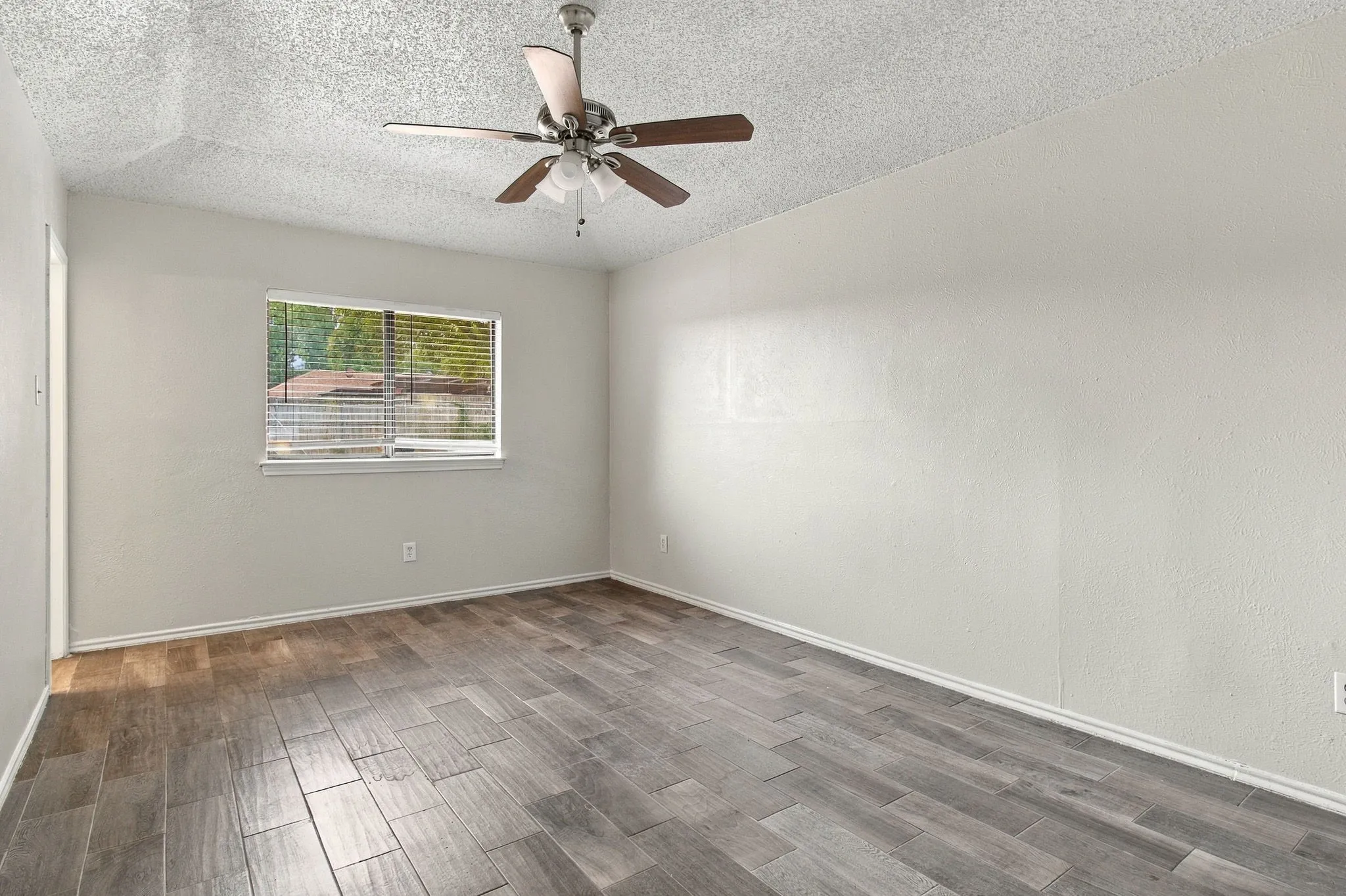Textured ceiling with a ceiling fan, light gray wall paint, white trim, wood-finish flooring, and a window with blinds