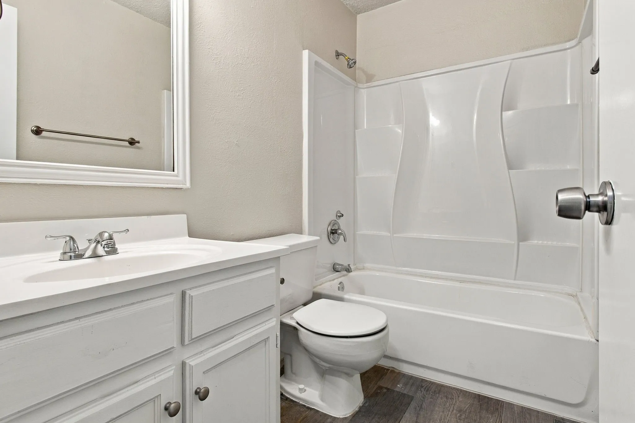 White vanity with an integrated sink, polished chrome faucet, framed mirror, and a white tub/shower combination with a textured surround