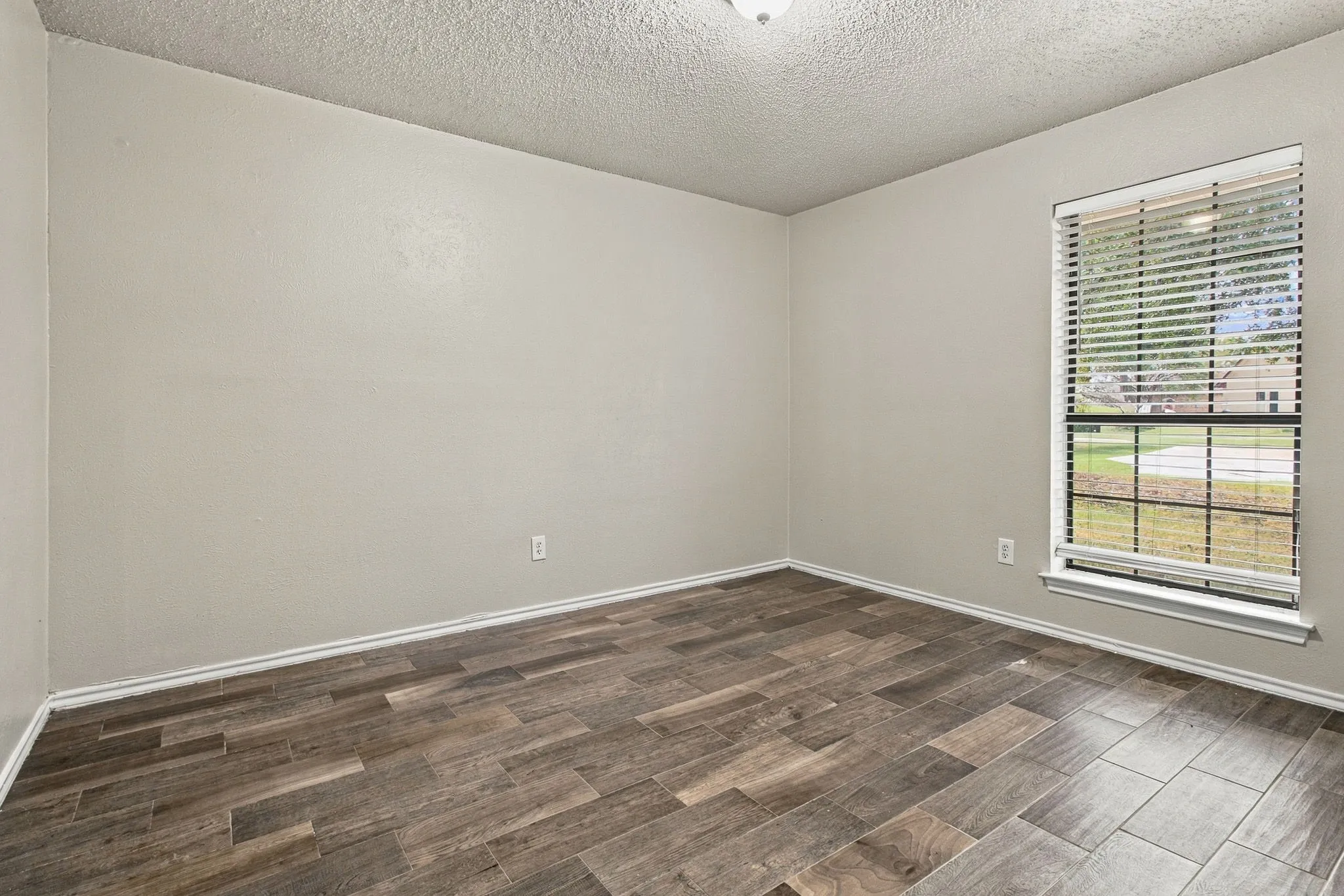 Wood-finish flooring, neutral wall tones, single window with blinds, and ceiling-mounted light fixture