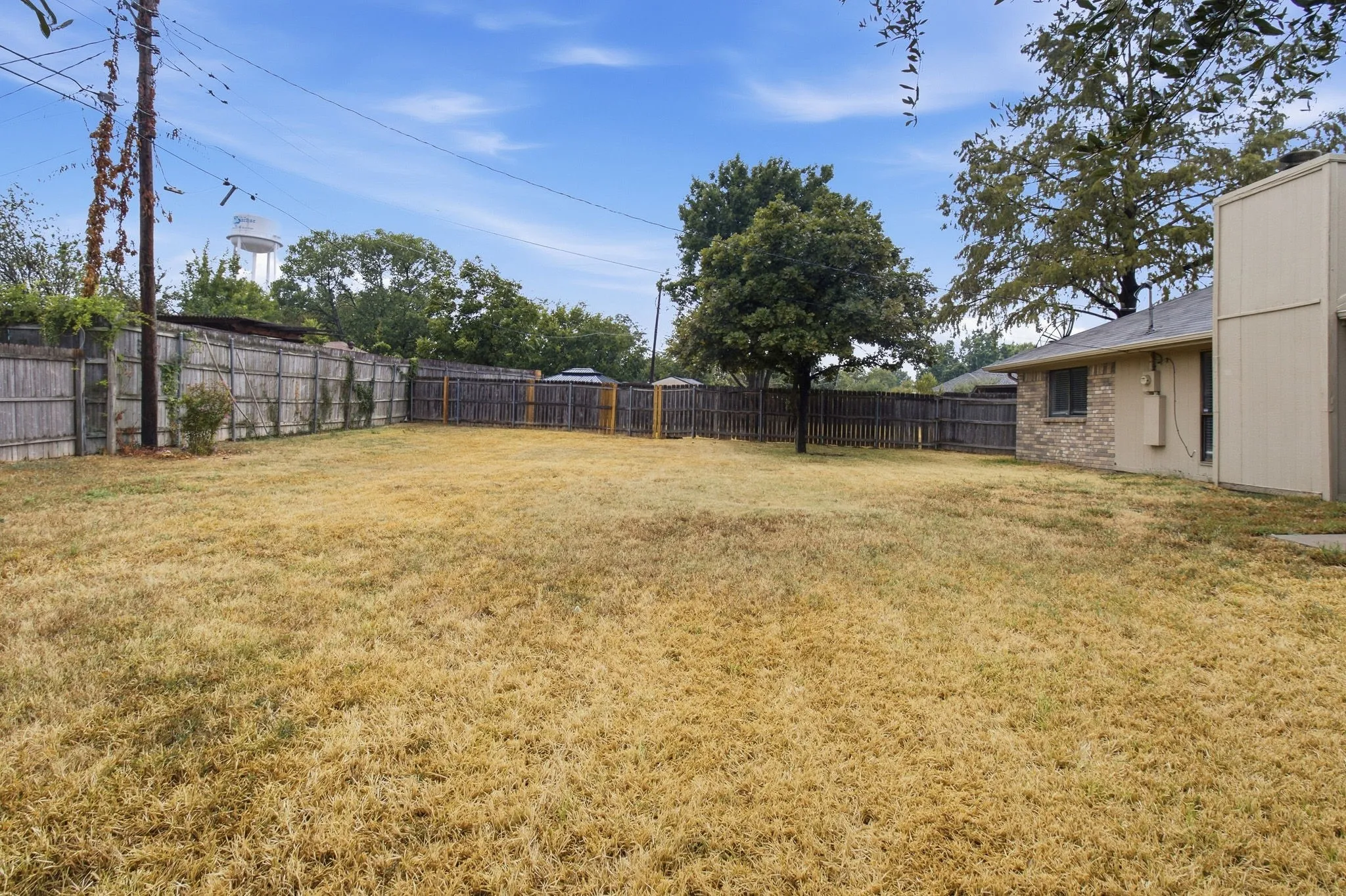 Expansive fenced yard featuring mature trees and a brick exterior