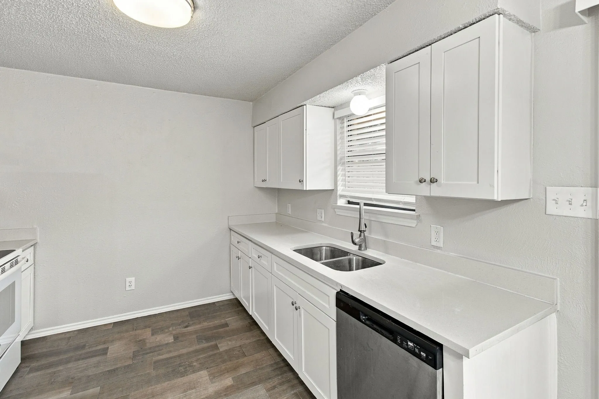White shaker-style cabinetry, light-toned countertops, stainless steel dual-basin sink, and wood-finish flooring