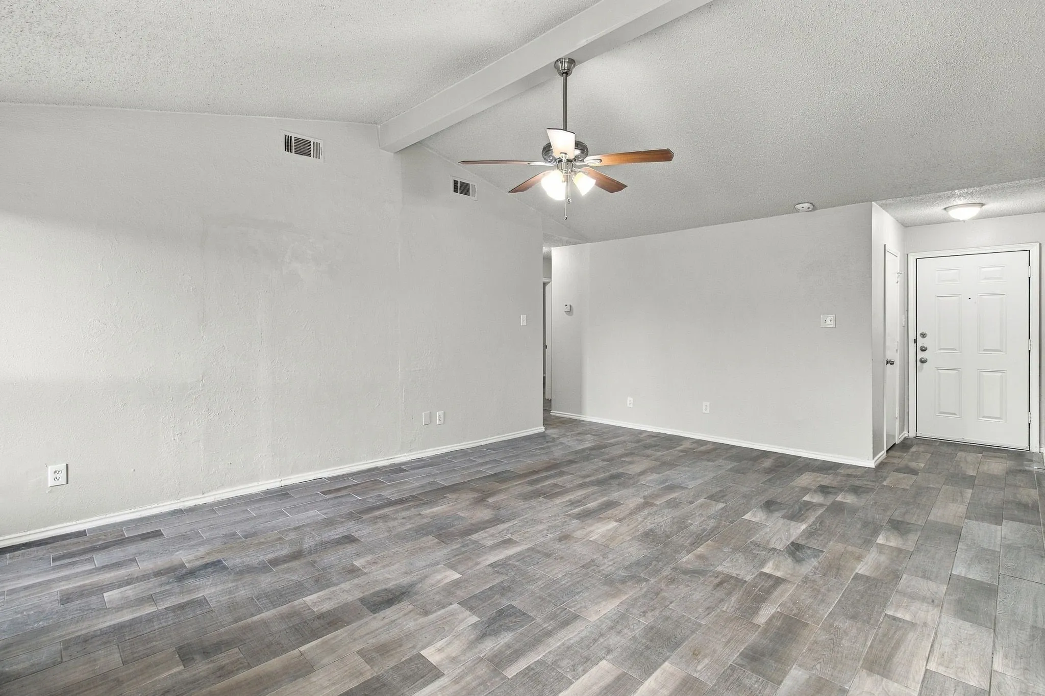 Vaulted ceiling with exposed beam, wood-finish flooring, ceiling fan with light fixture, and white paneled entry door