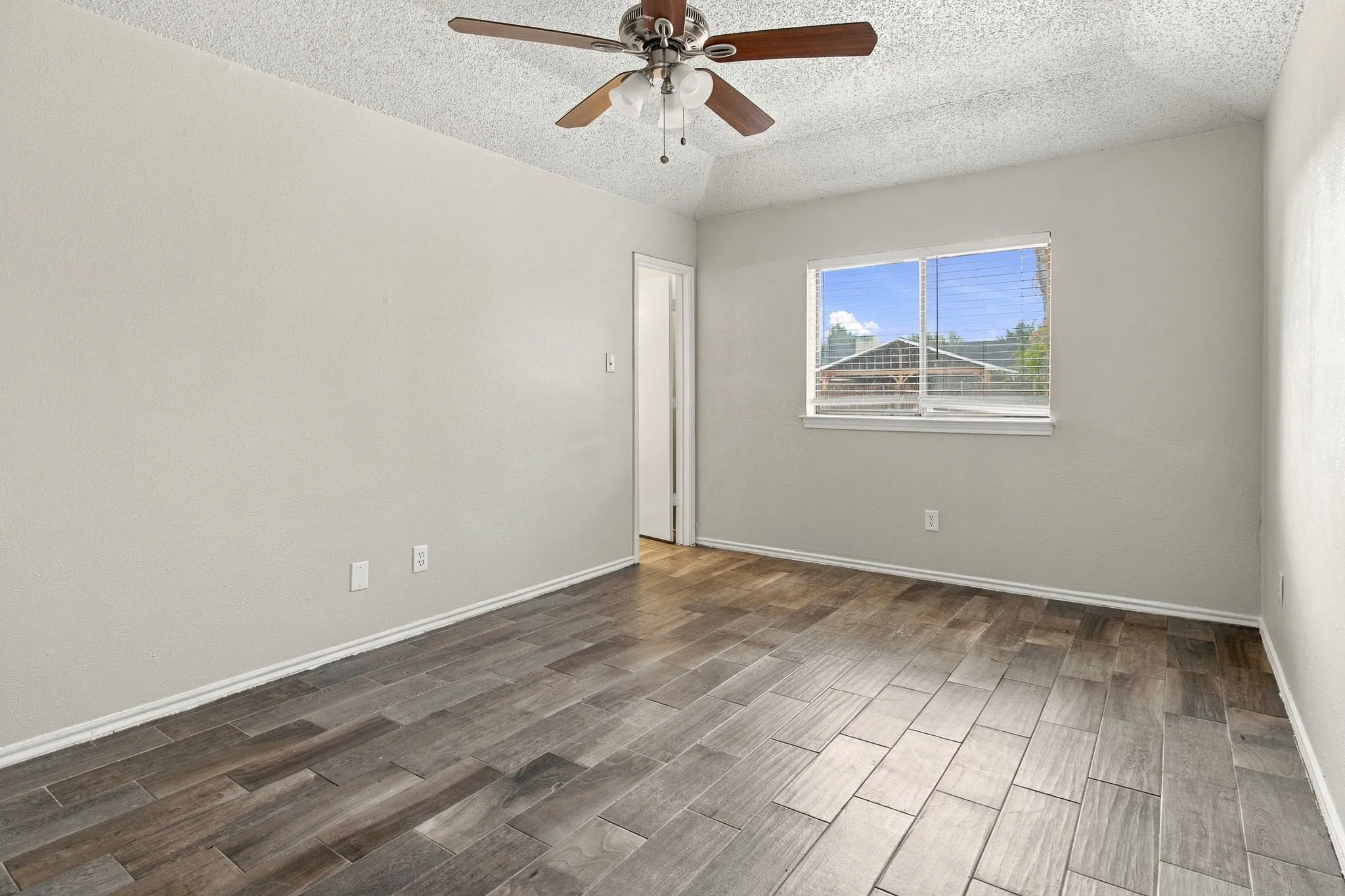 Wood-finish tile flooring, ceiling fan with integrated lighting, and multiple windows with blinds
