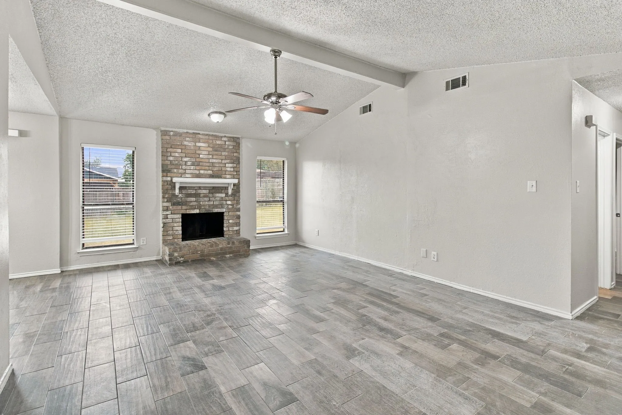 Living area with vaulted ceilings, a brick fireplace with mantel, and wood-look tile flooring