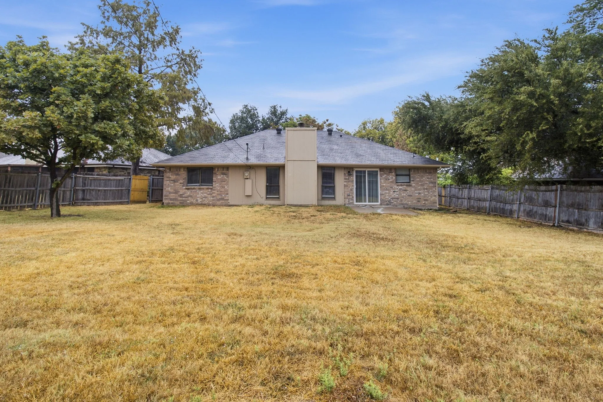 Expansive backyard featuring a brick exterior, sliding glass door, and a privacy fence