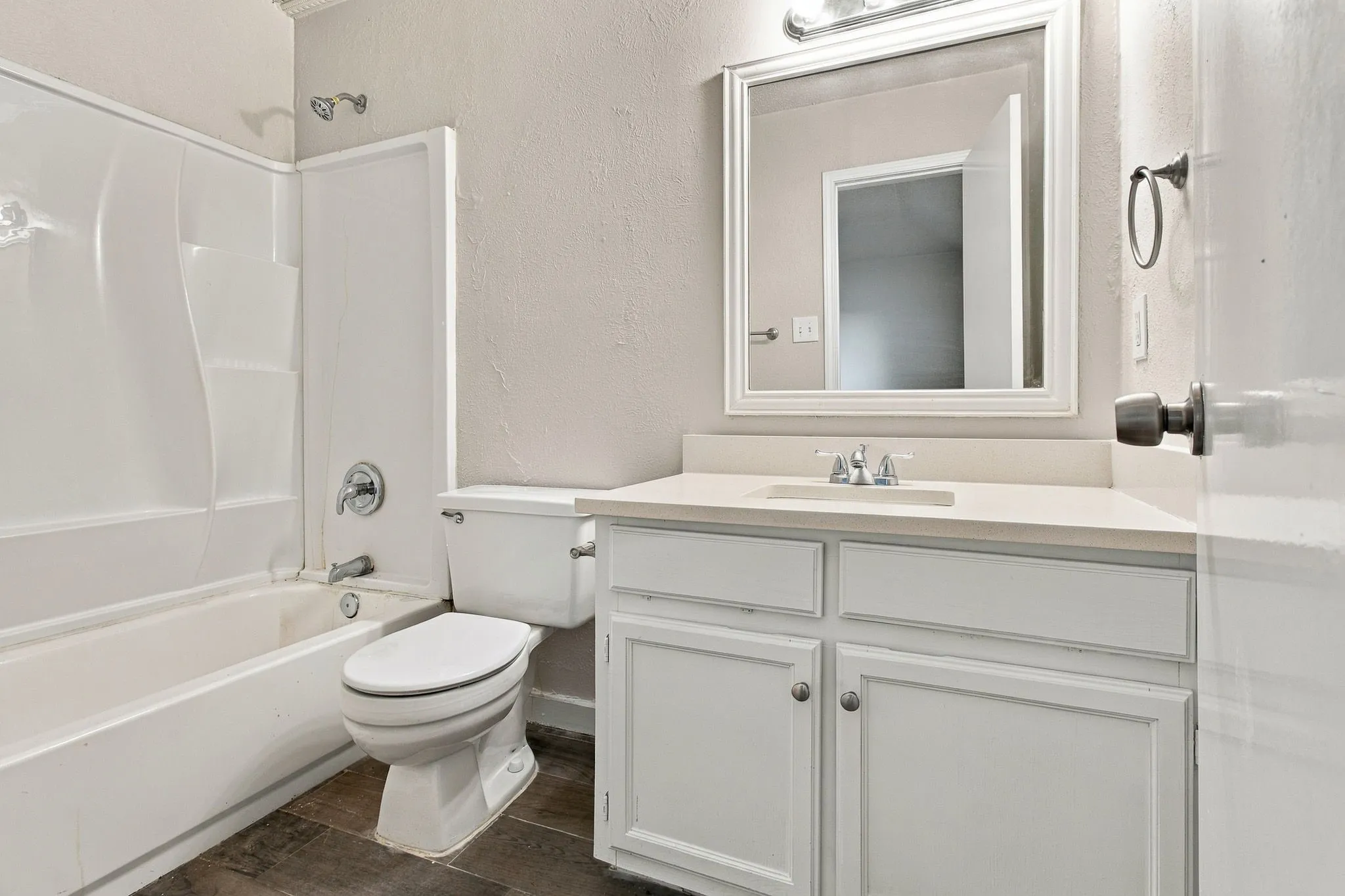 White vanity with a light-toned countertop, framed mirror, and a shower-over-tub combination