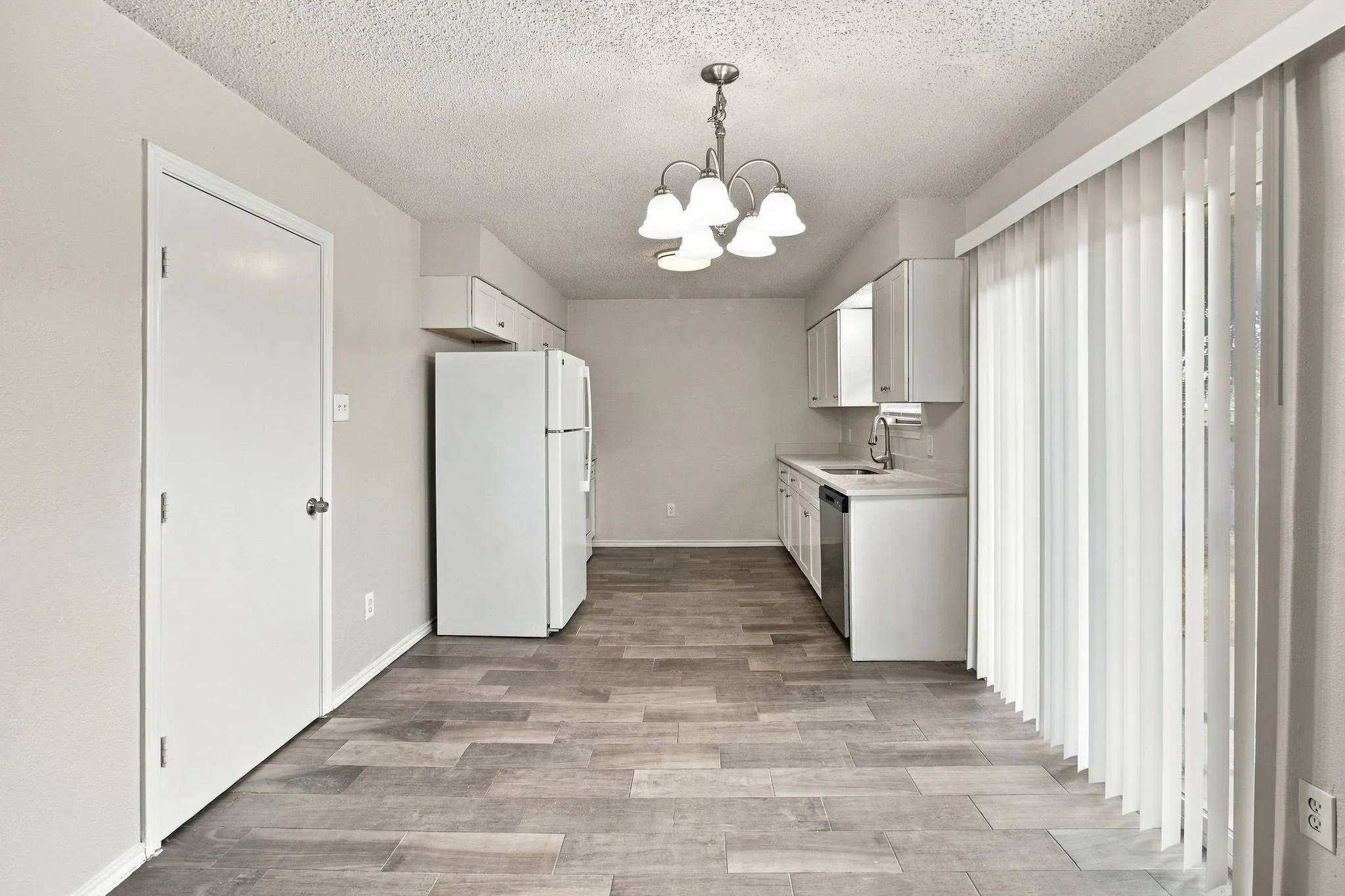 Kitchen with wood-finish flooring, white cabinetry, white appliances, and a hanging chandelier