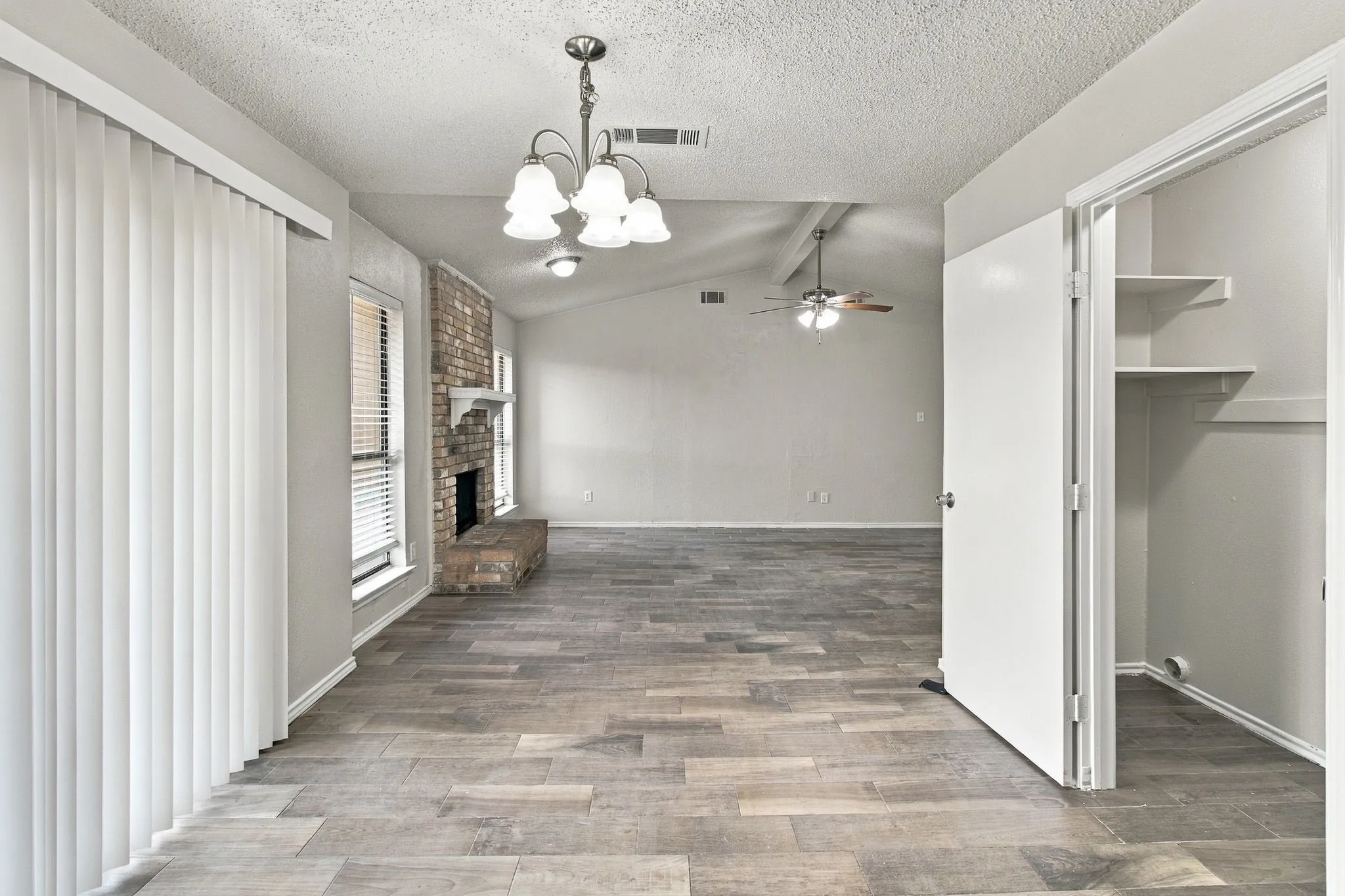 Vaulted ceiling with a ceiling fan, brick fireplace, wood-finish flooring, and built-in closet shelving