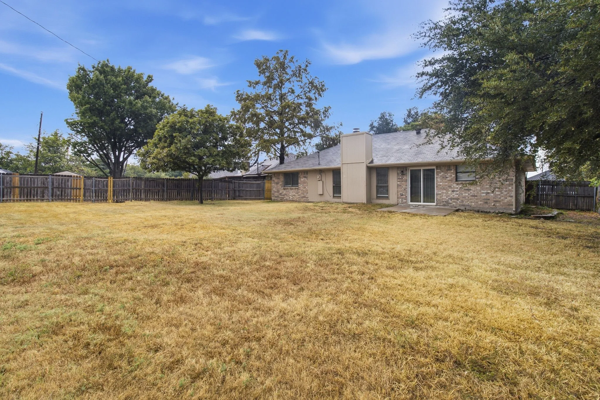 Expansive backyard featuring a wood privacy fence, mature trees, and a concrete patio