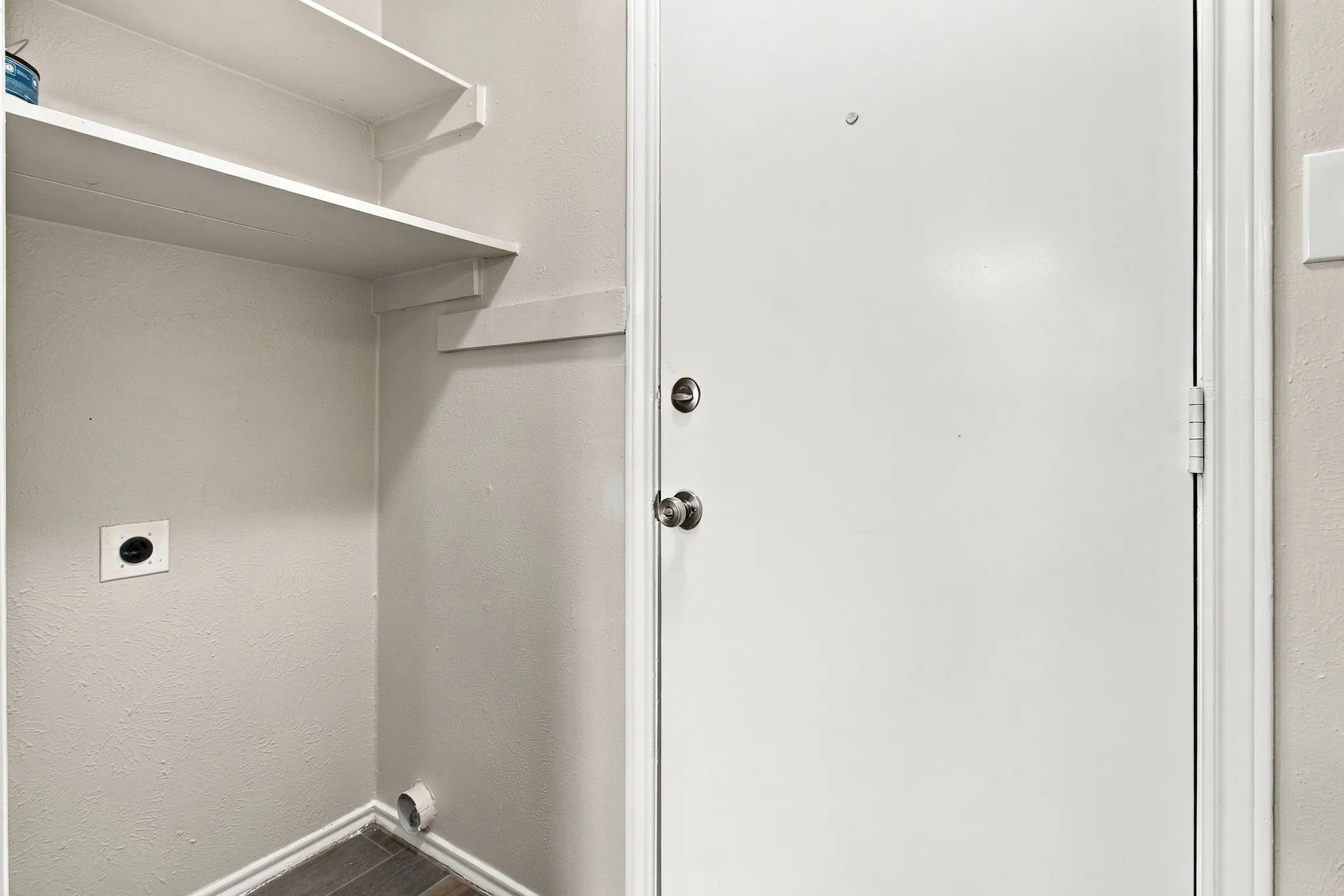 Utility area with wood-finish flooring, wall-mounted shelving, and a white entry door