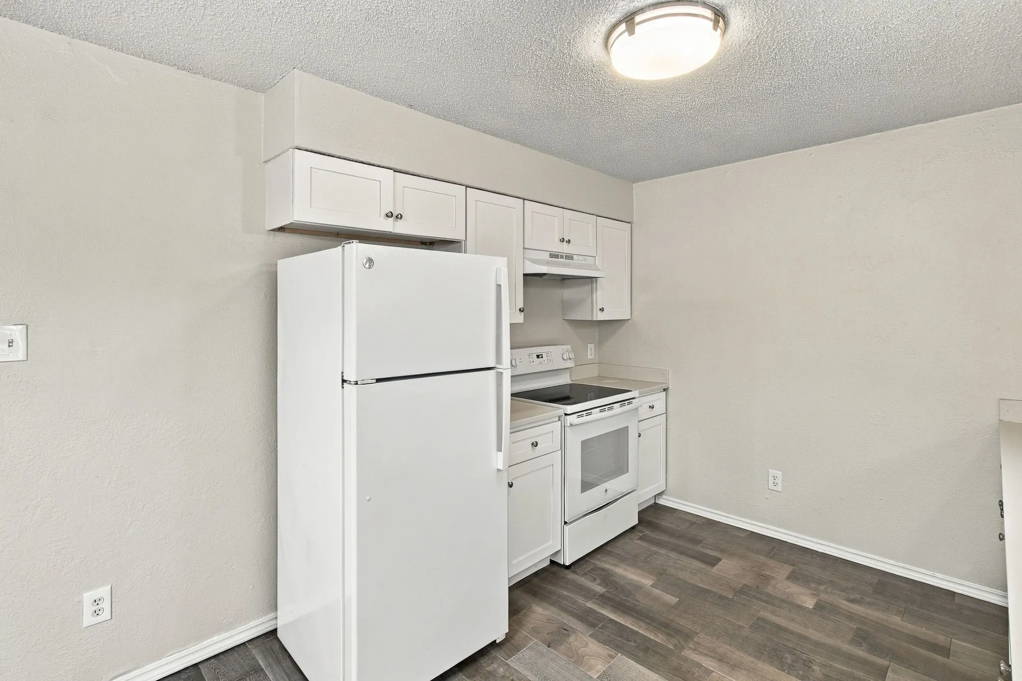 Kitchen featuring white cabinetry, wood-finish flooring, and white appliances including a refrigerator and electric range