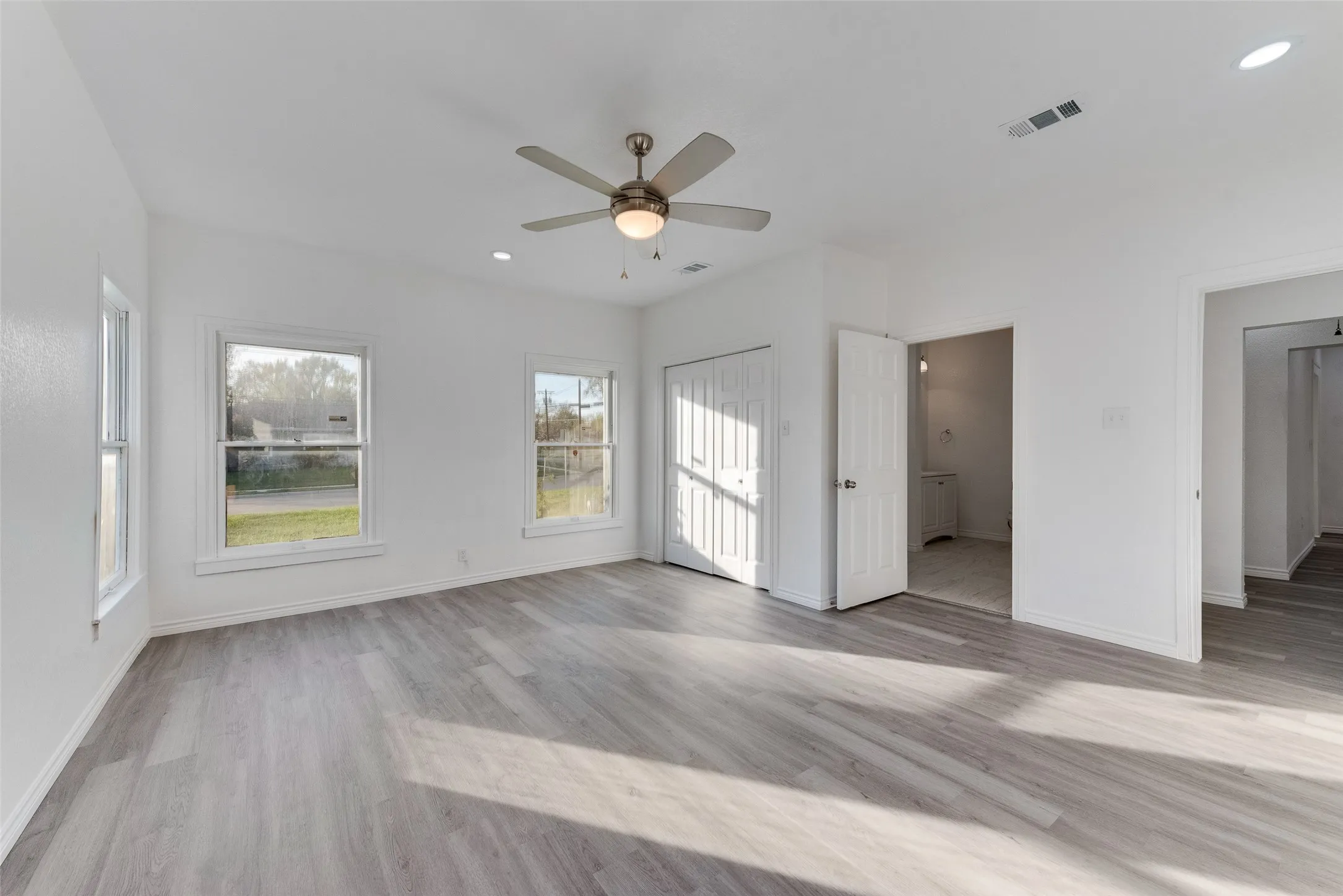 Spacious room featuring wood-finish flooring, multiple windows, a ceiling fan with integrated lighting, and a bi-fold closet
