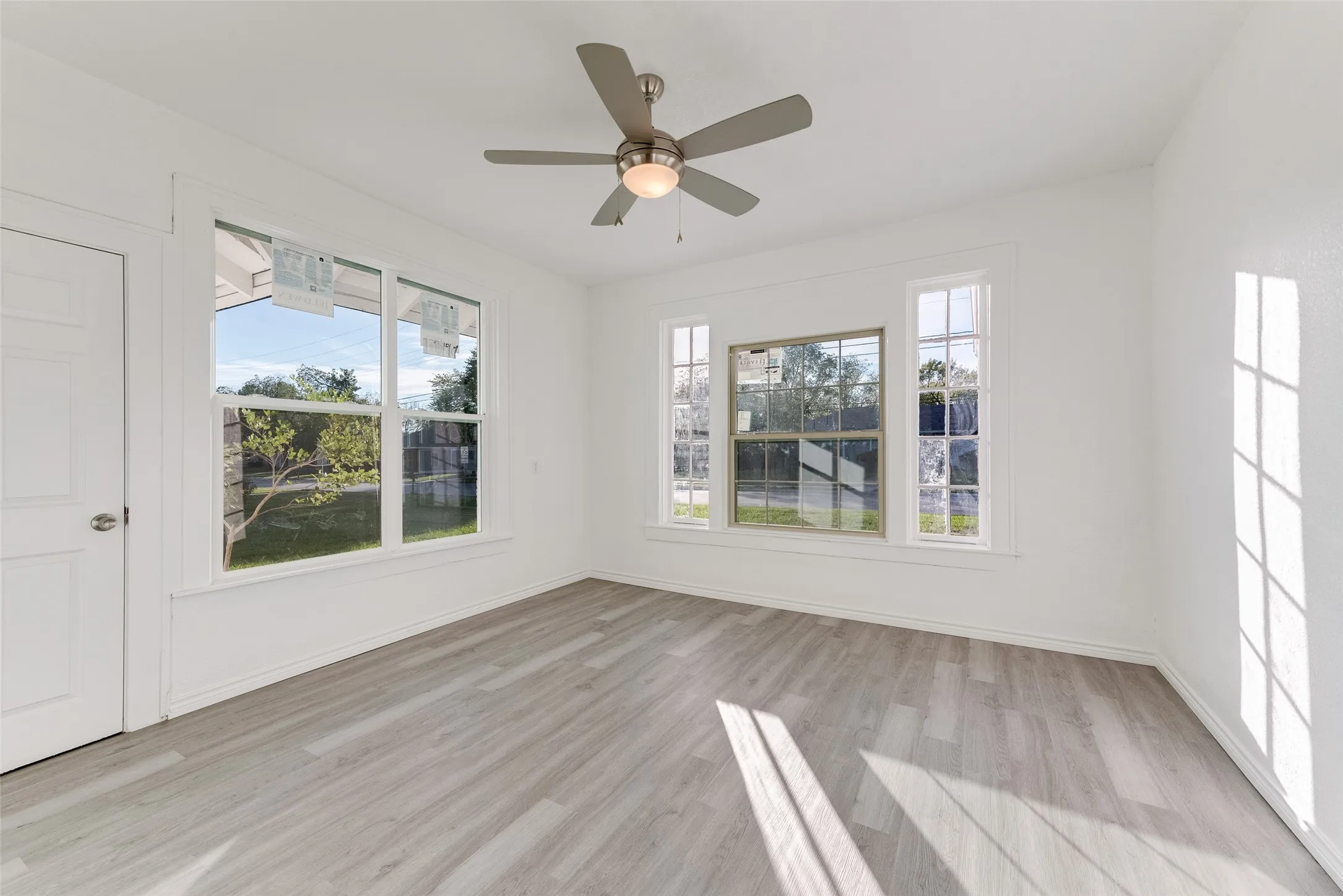 Wood-finish flooring, multiple windows, ceiling fan, and white painted walls