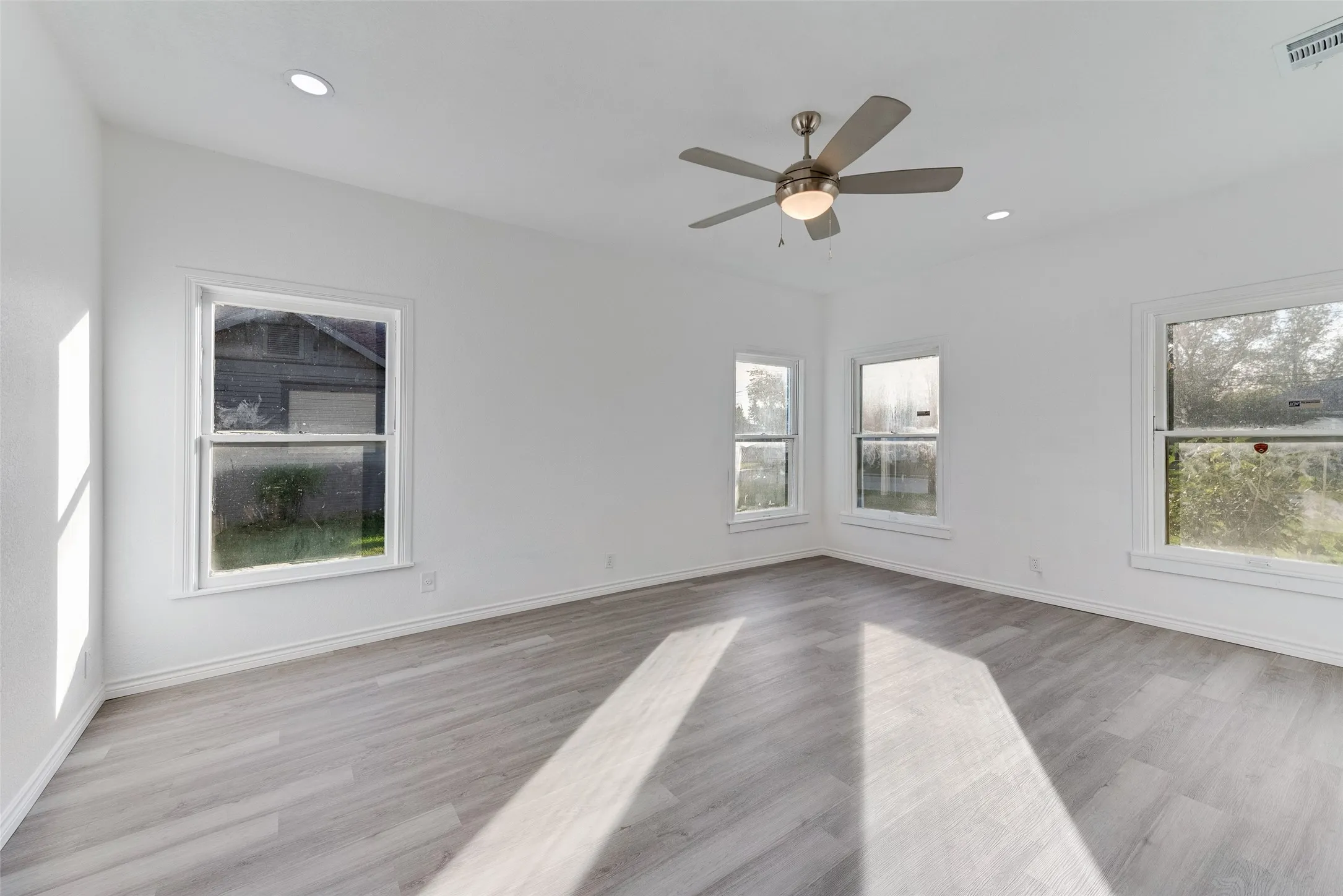 Recessed lighting, ceiling fan, white wall finish, multiple windows, and wood-finish flooring