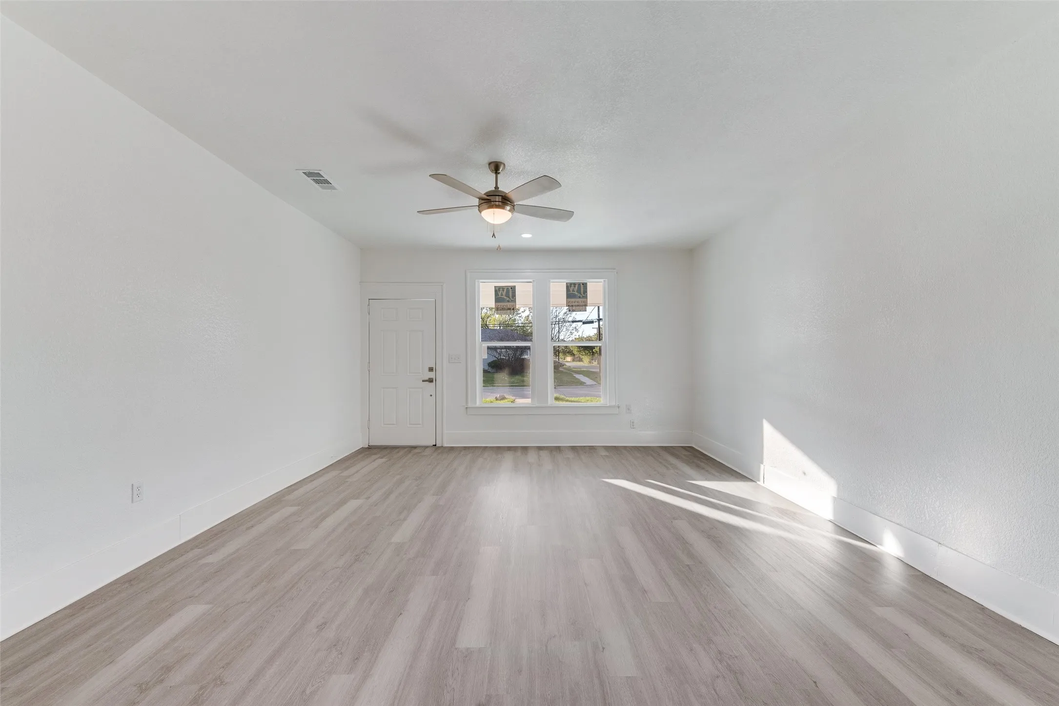 Spacious room featuring wood-finish flooring, a ceiling fan, and two windows