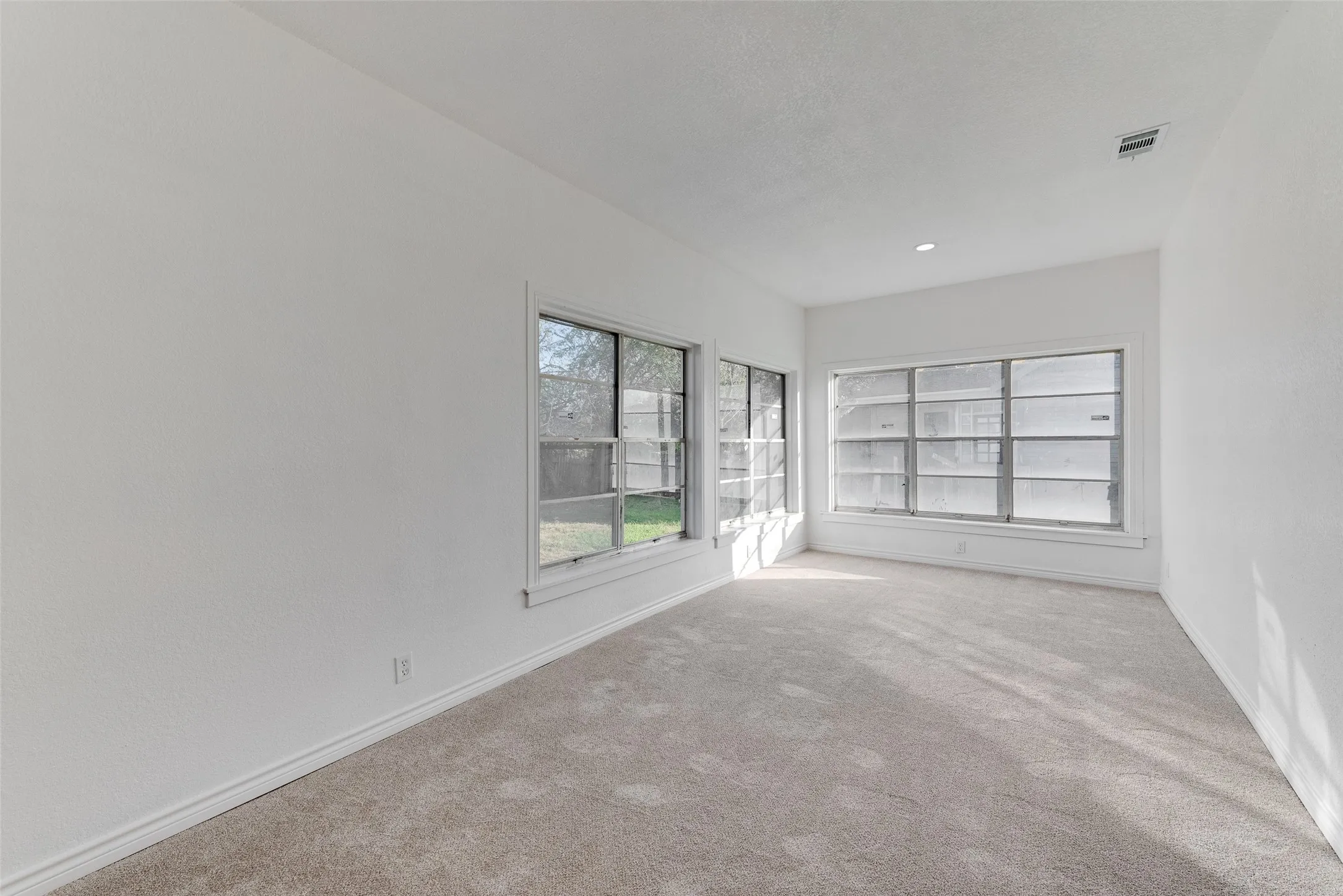 Neutral tone wall paint, recessed lighting, multiple windows, carpet flooring, and white trim