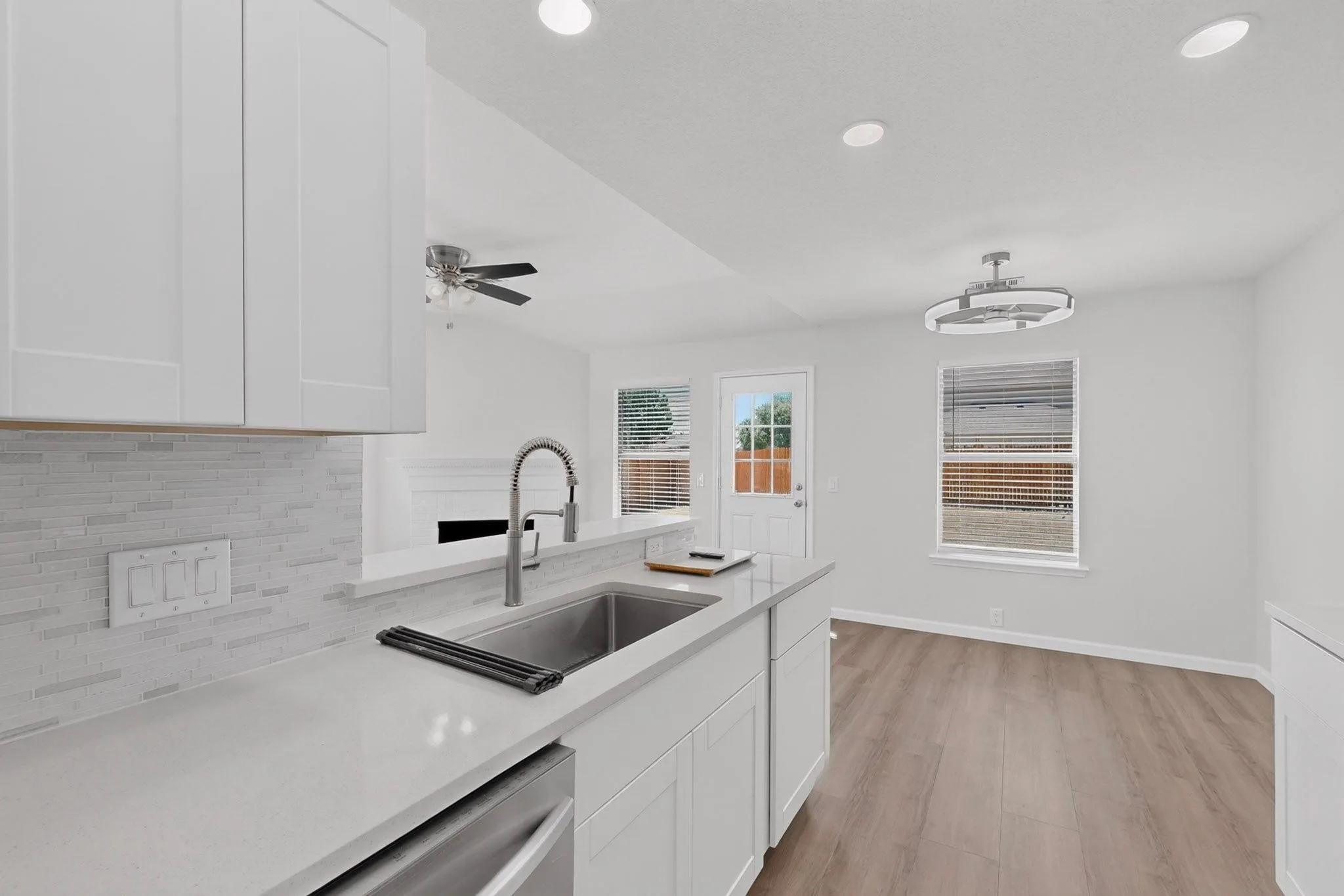 Kitchen featuring white shaker cabinetry, light-toned countertops, a stainless steel sink with a gooseneck faucet, and a mosaic tile backsplash