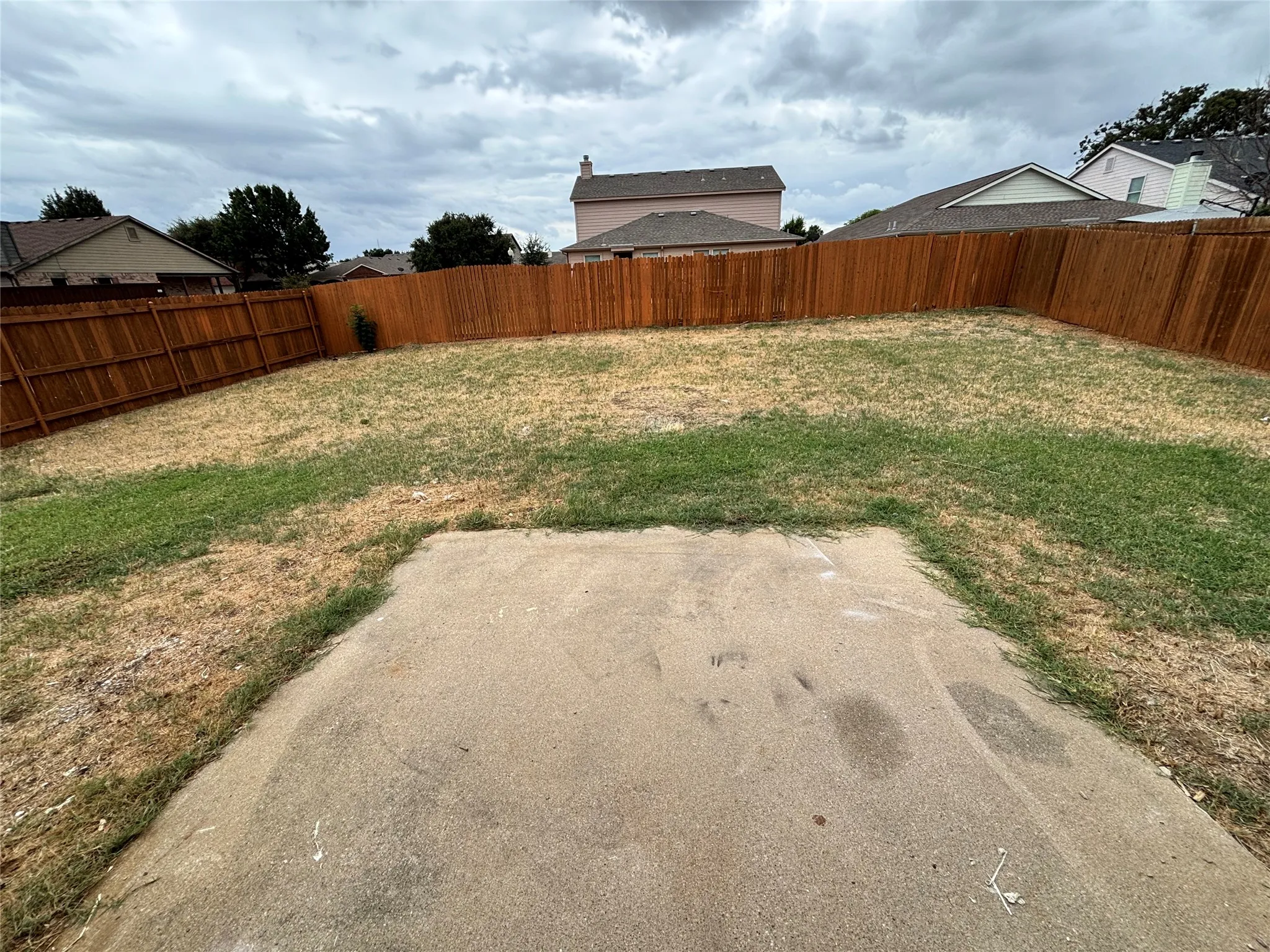 Fenced backyard featuring a concrete patio and perimeter wood fencing