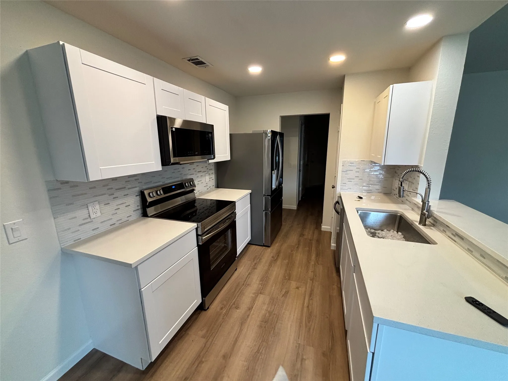 Modern kitchen featuring white shaker cabinetry, stainless steel appliances, light-toned countertops, a mosaic tile backsplash, and wood-finish flooring