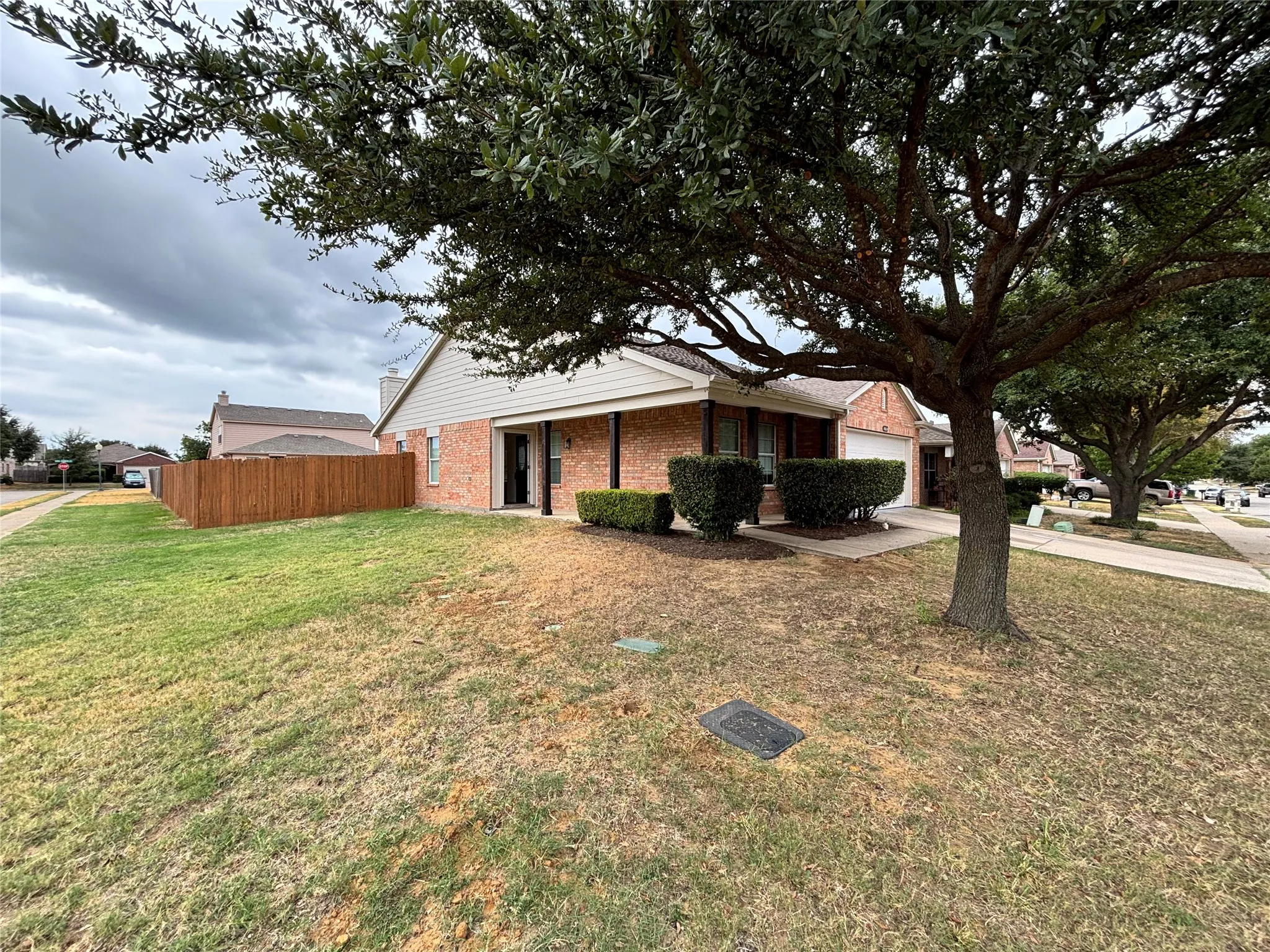 Brick exterior with siding accents, attached garage, mature tree, and a wooden privacy fence