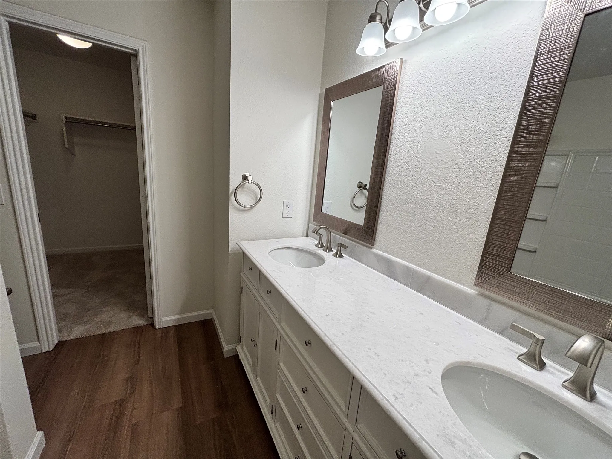 Dual vanity with white cabinetry and integrated sinks, brushed nickel fixtures, wood-finish flooring, and framed mirrors