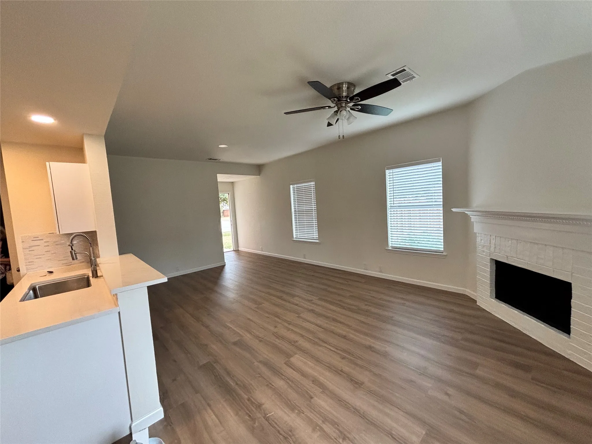 Vaulted ceilings, wood-finish flooring, white brick fireplace, stainless steel sink, and a ceiling fan with light fixture