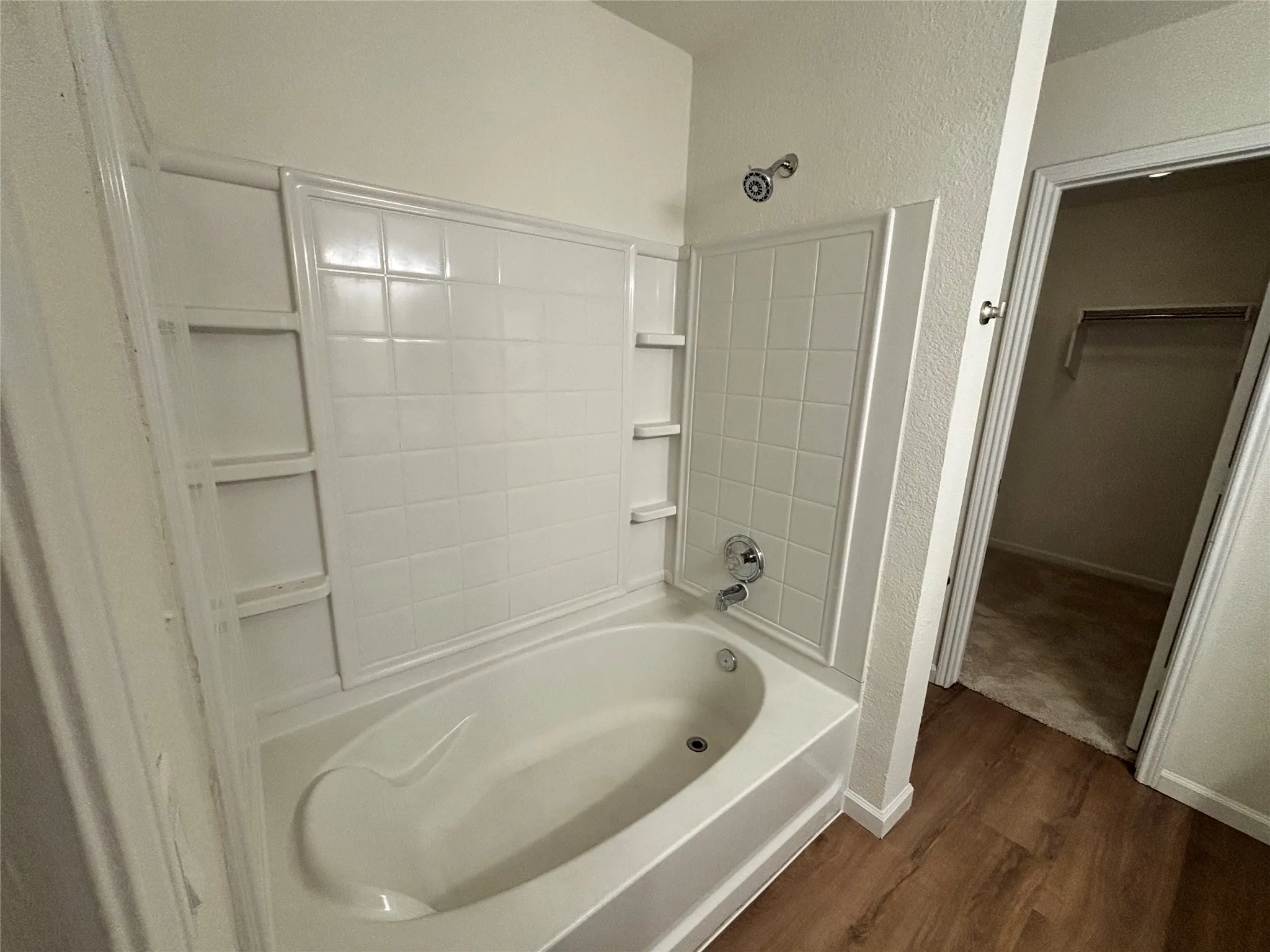 Tub and shower combination with white tile-patterned surround, integrated shelving, and polished chrome fixtures