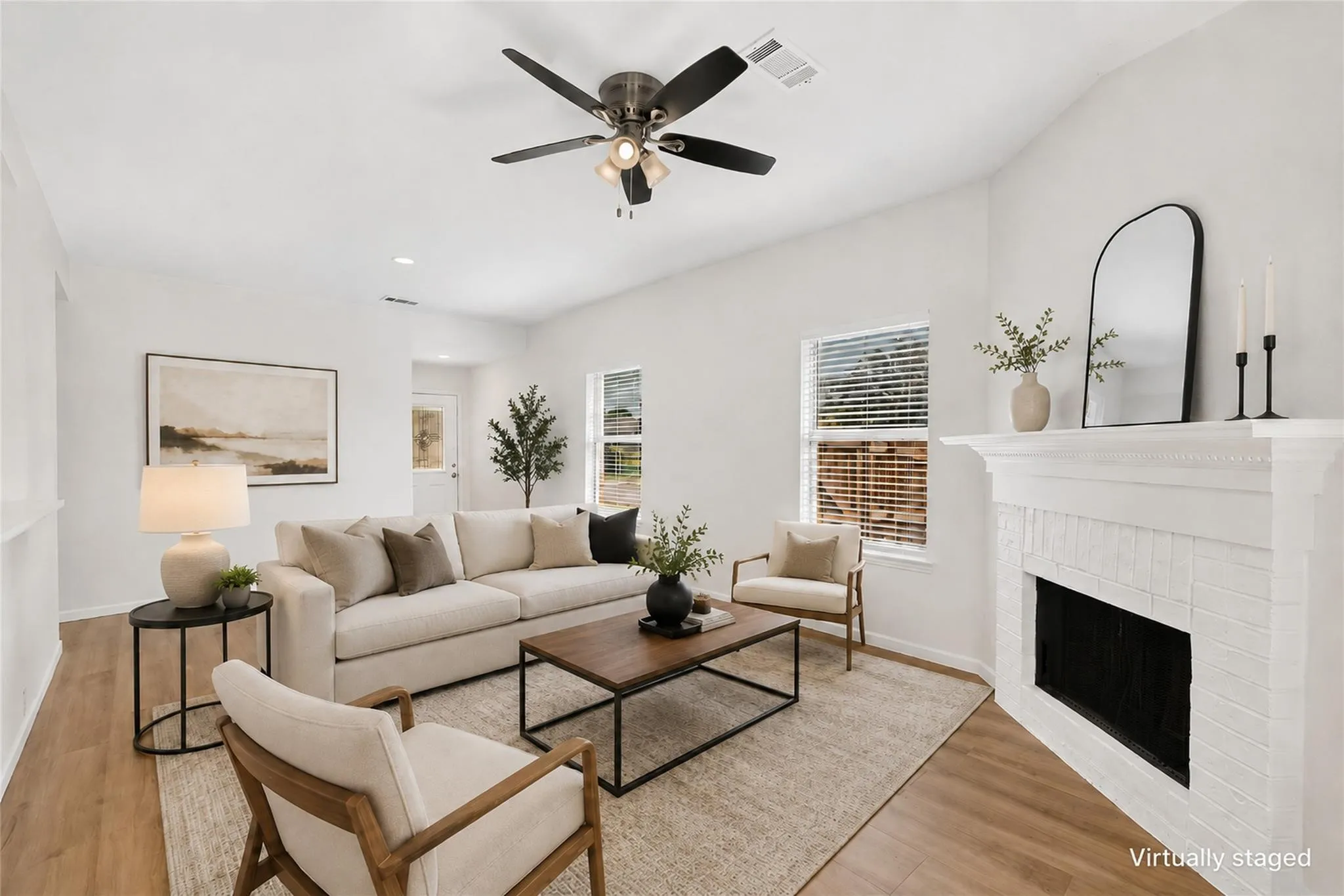 Vaulted ceiling with a ceiling fan, white painted brick fireplace with a mantel, wood-finish flooring, and multiple windows
