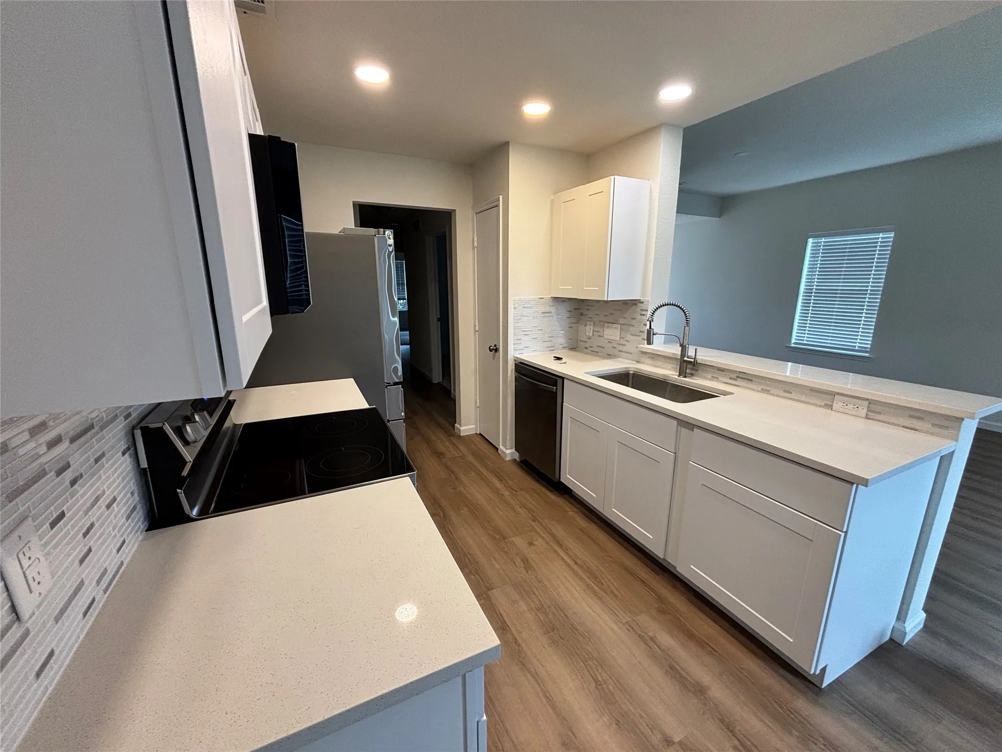 Modern kitchen with light cabinetry, light countertops, wood-finish flooring, stainless steel appliances, and a tiled backsplash