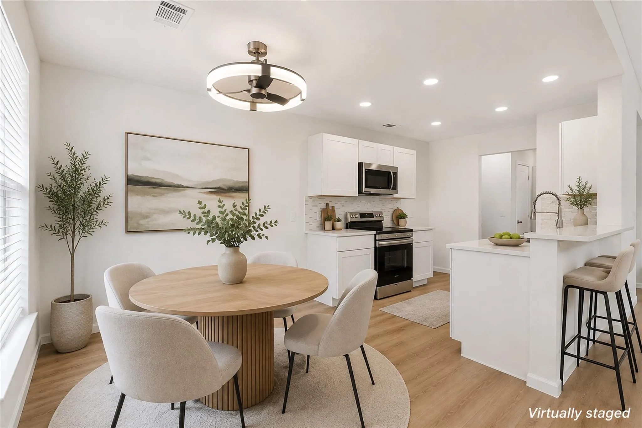 Open-concept living space with wood-finish flooring, white cabinetry, stainless steel appliances, and recessed lighting