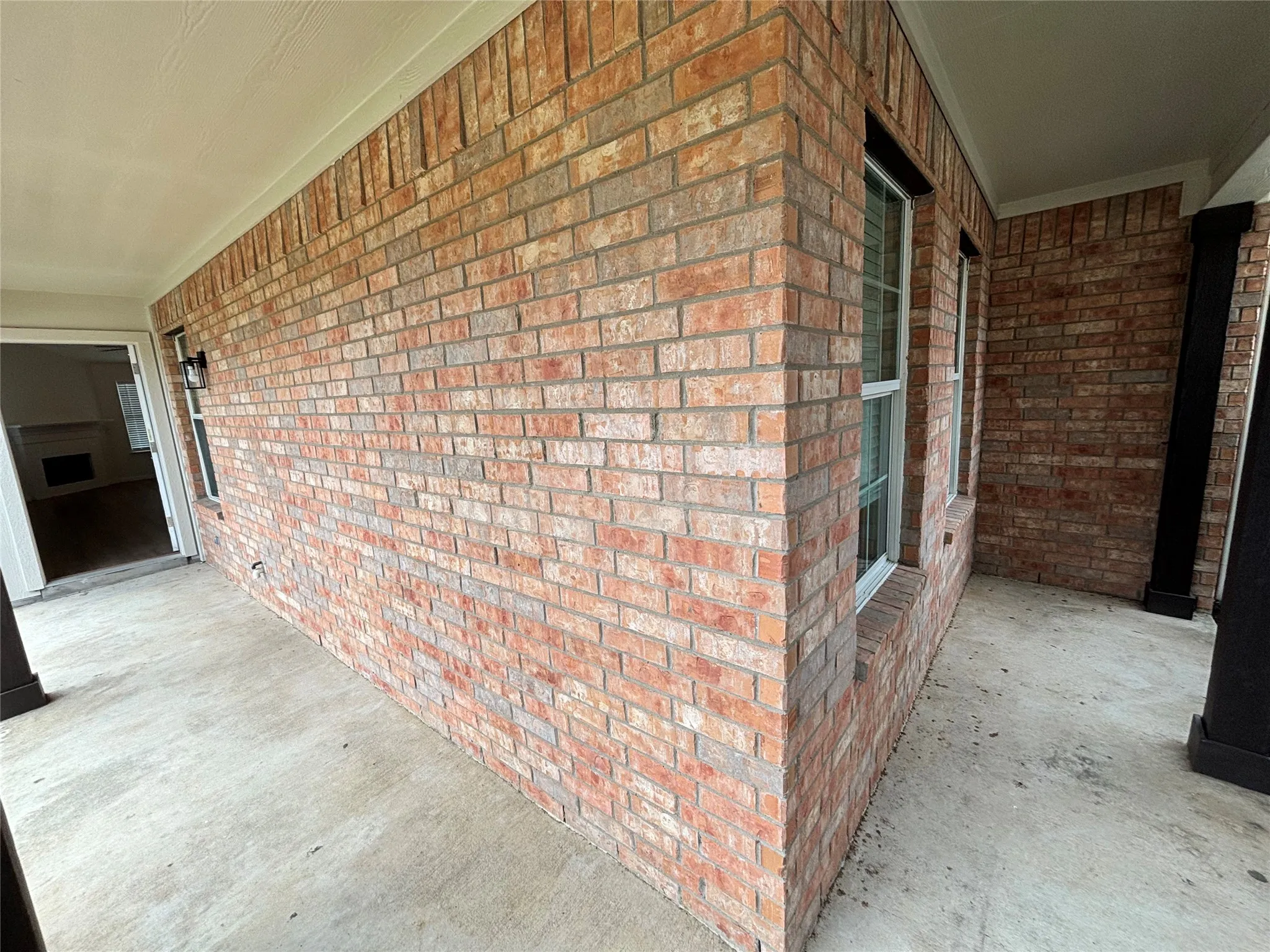 Brick exterior with covered concrete patio, white framed windows, and exterior lighting fixture