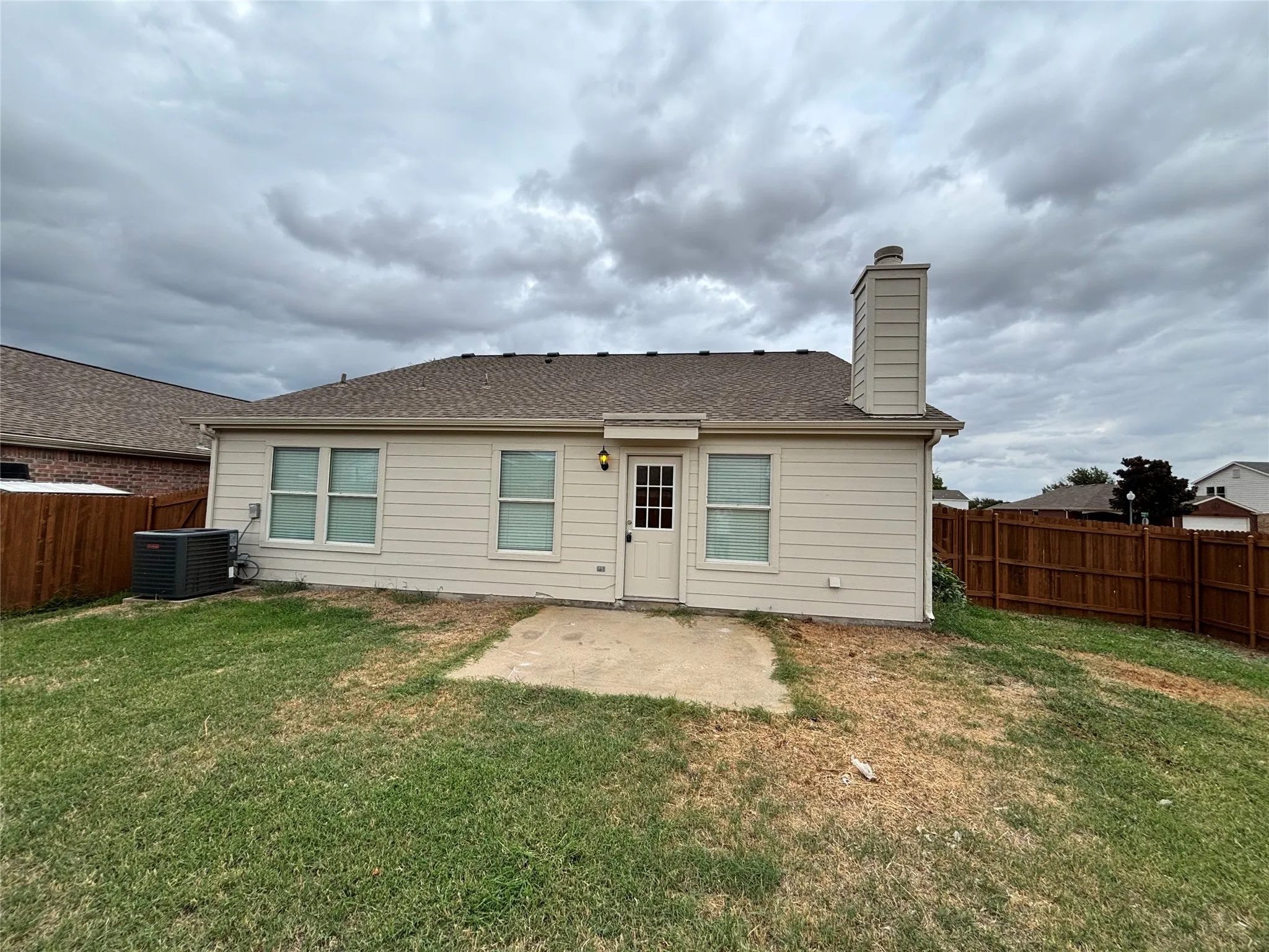 Rear exterior featuring siding, an attached chimney, multiple windows, a rear entry door, and a privacy fence