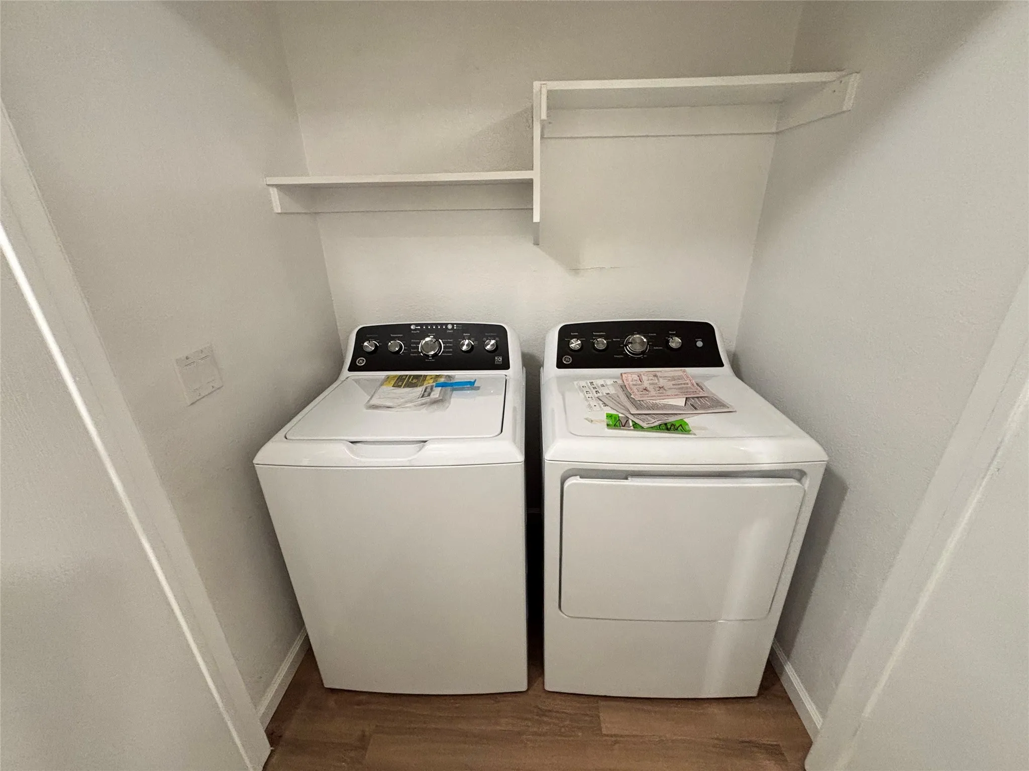 Laundry area with wood-finish flooring, white built-in shelving, and included washer and dryer appliances