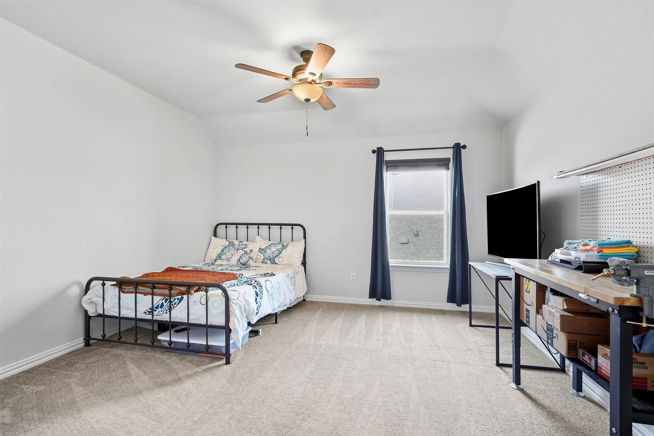 Carpeted room with a ceiling fan, a window, and a built-in pegboard wall
